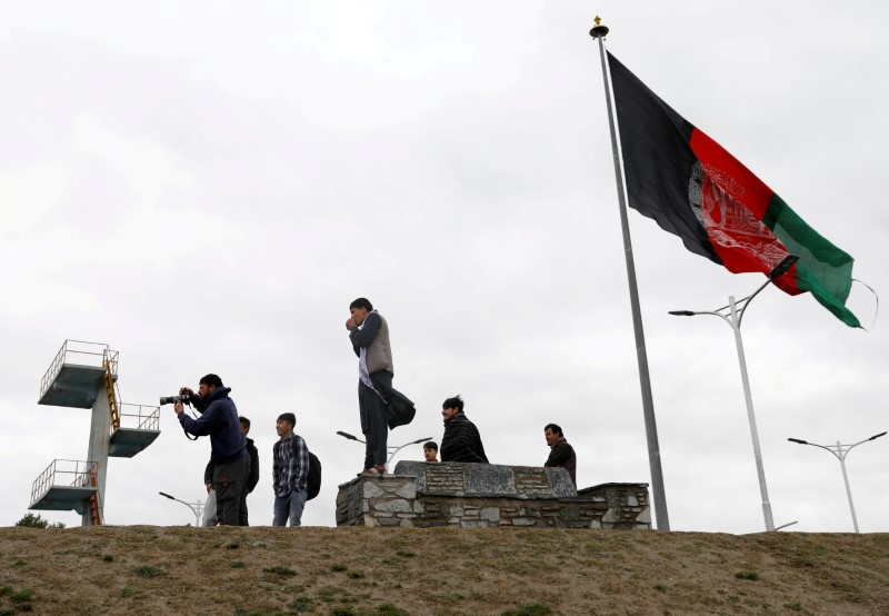 Youths take pictures next to an Afghan flag on a hilltop overlooking Kabul, Afghanistan, April 15, 2021. REUTERS/Mohammad Ismail/File Photo