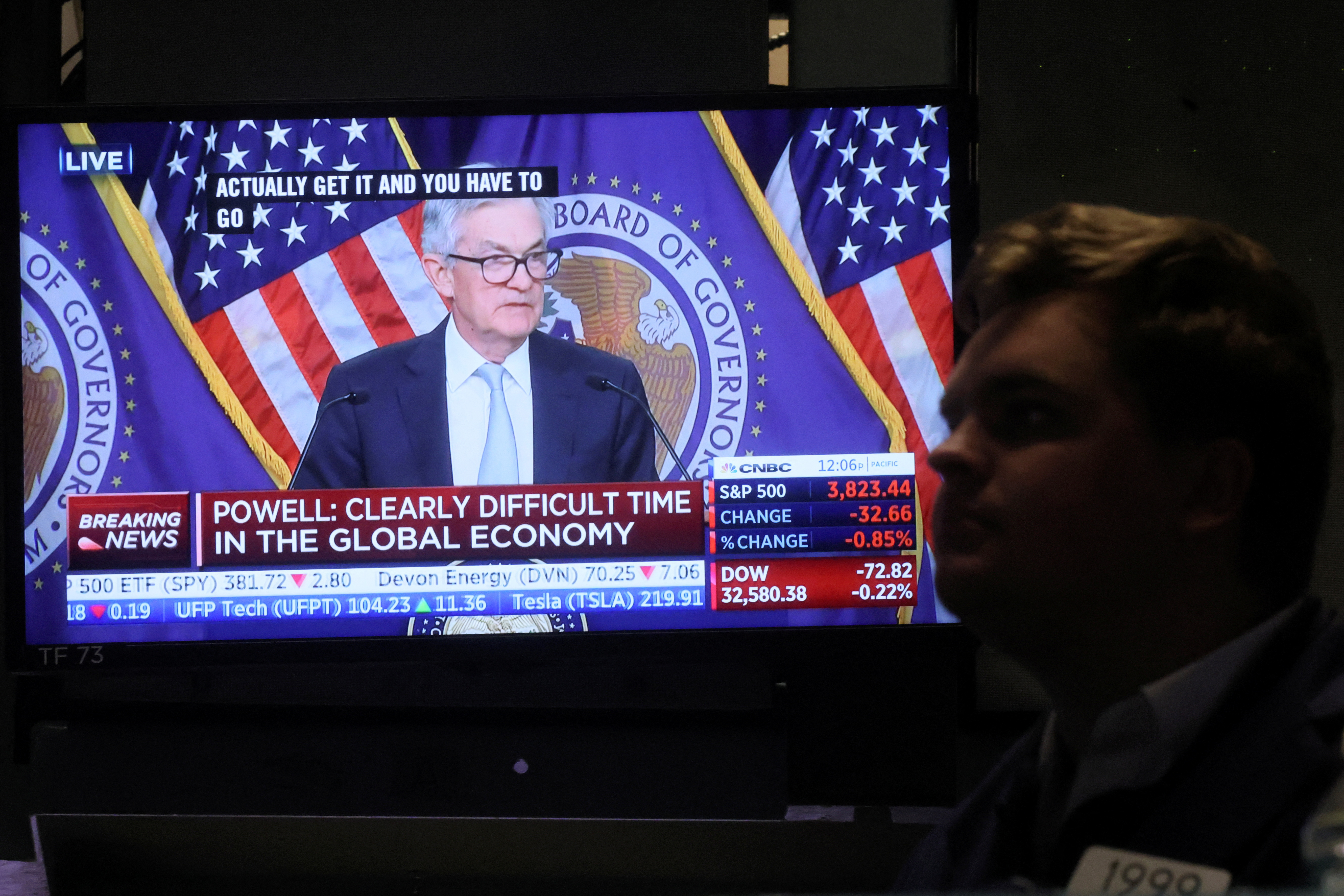 A screen displays Federal Reserve Chair Powell speaking as a trader works on the floor of the NYSE in New York