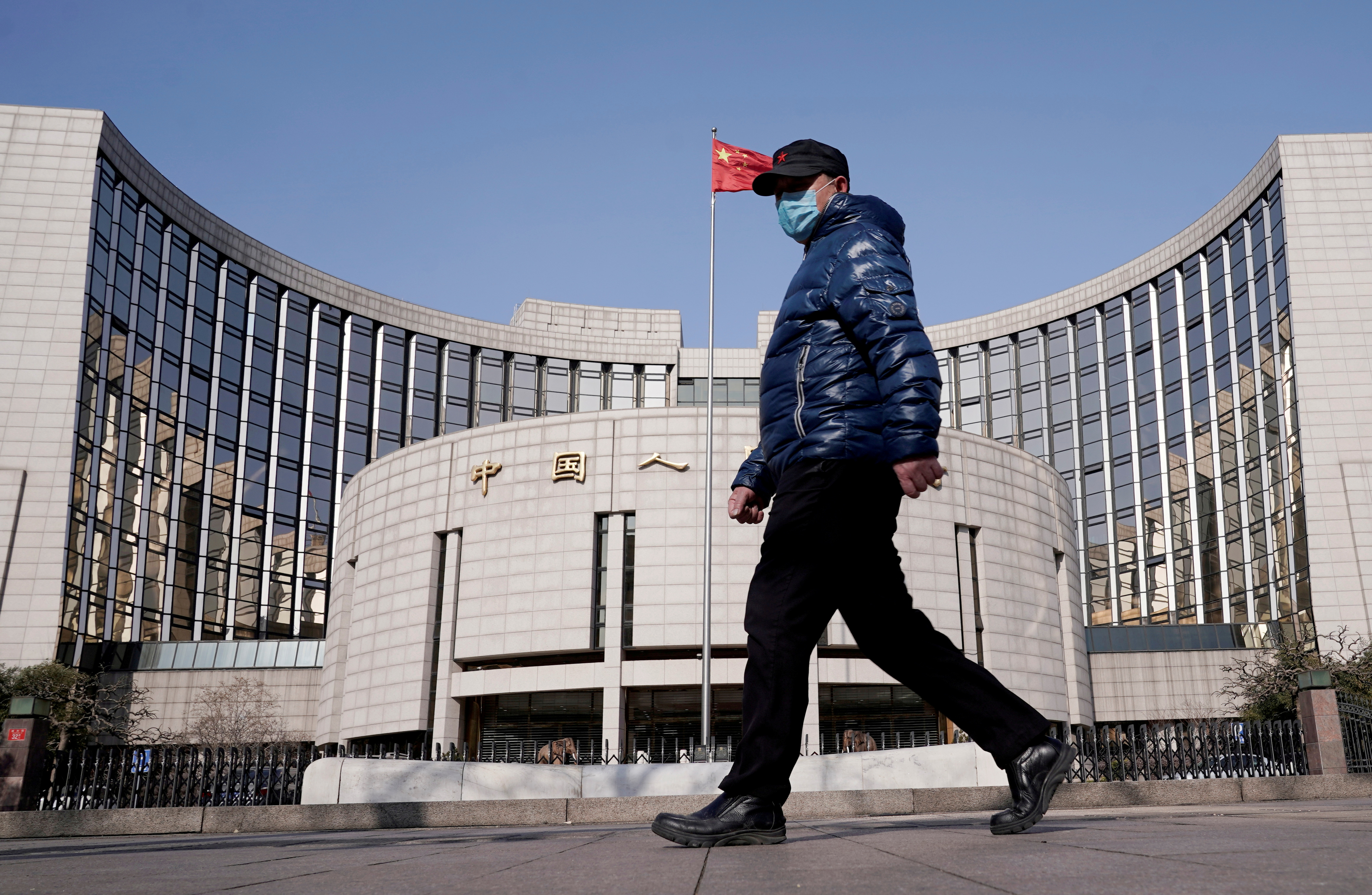 FILE PHOTO: A man wearing a mask walks past the headquarters of the People's Bank of China, the central bank, in Beijing, China, February 3, 2020. REUTERS/Jason Lee/File Photo/File Photo
