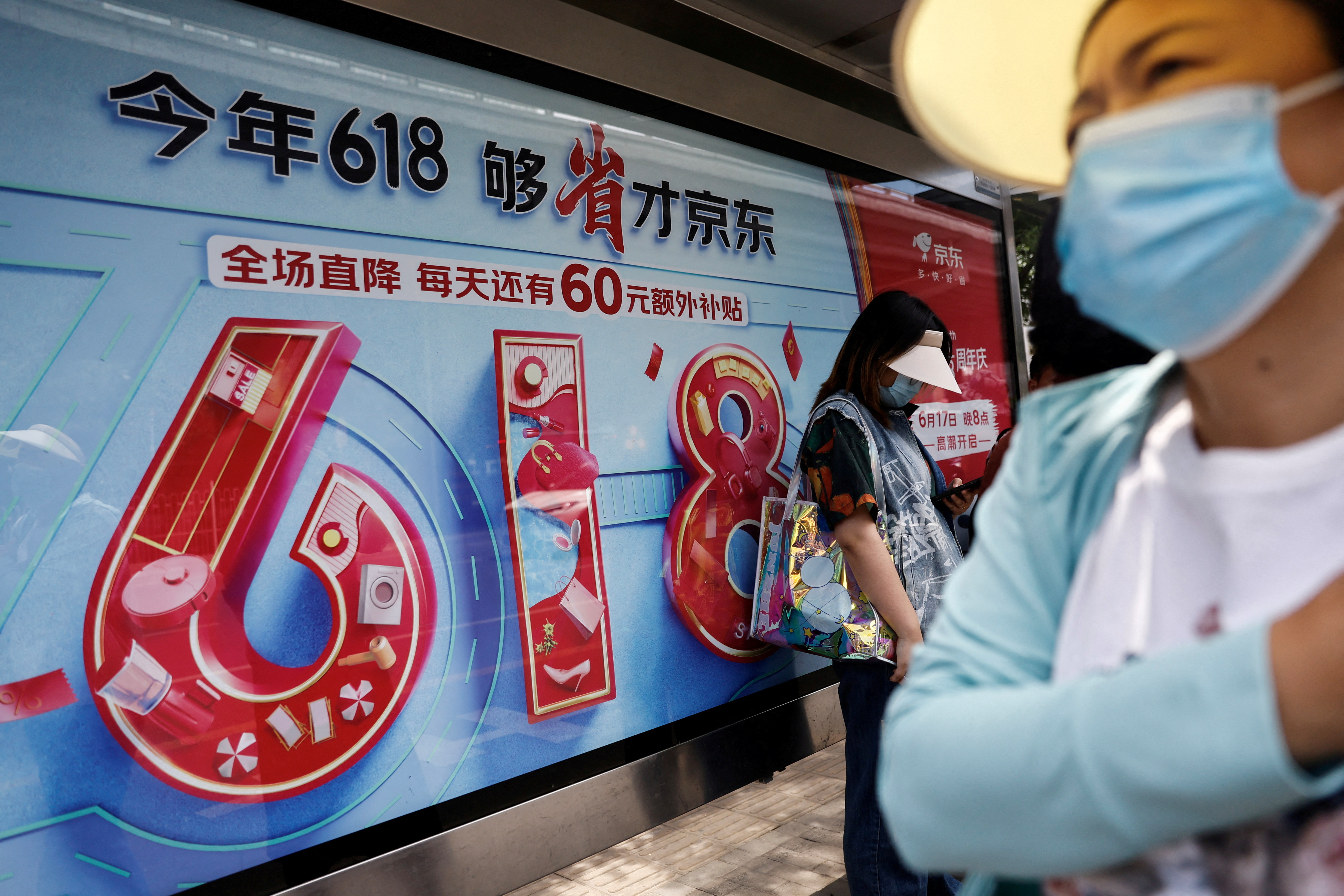 People wait for bus near a billboard of JD.com advertisement for the 