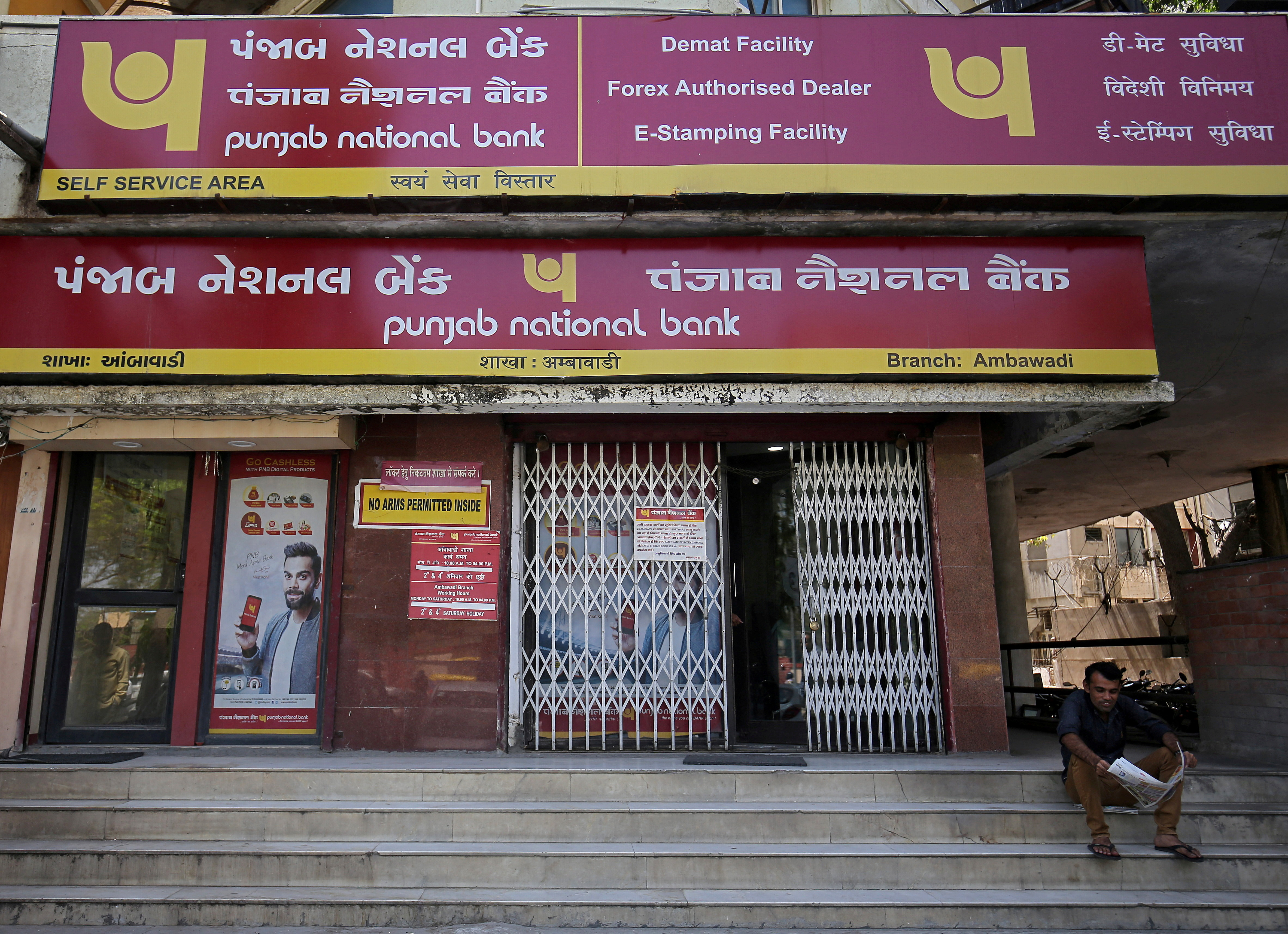 A man reads a newspaper outside a branch of Punjab National Bank in Ahmedabad