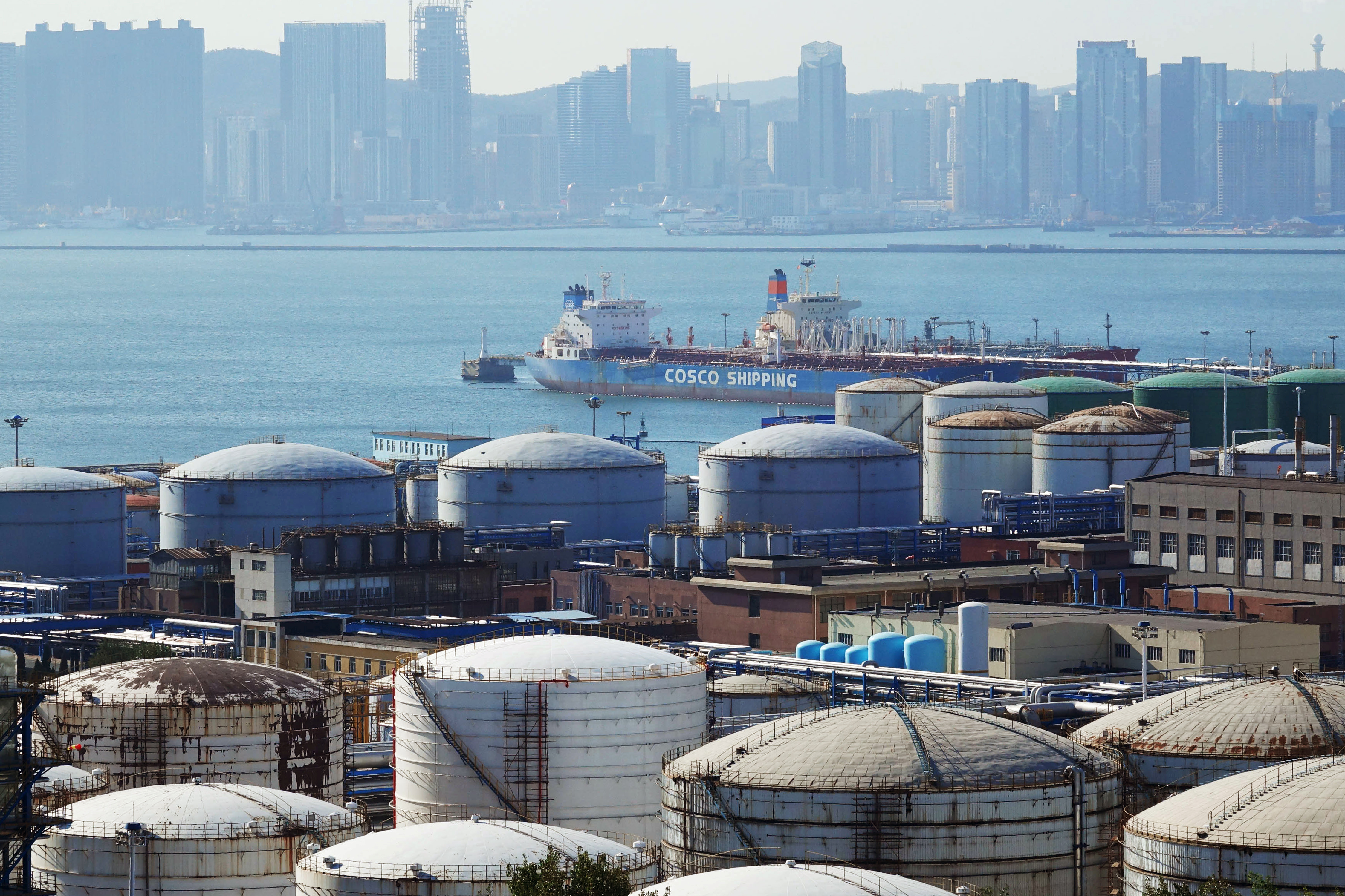 A China Ocean Shipping Company (COSCO) vessel is seen near oil tanks at the China National Petroleum Corporation (CNPC)'s Dalian Petrochemical Corp in Dalian, Liaoning province, China October 15, 2019. REUTERS/Stringer.