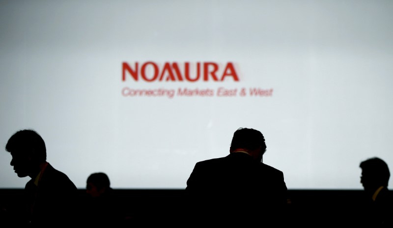 Investors stand in front of a screen showing the logo of Nomura Holdings in Tokyo
