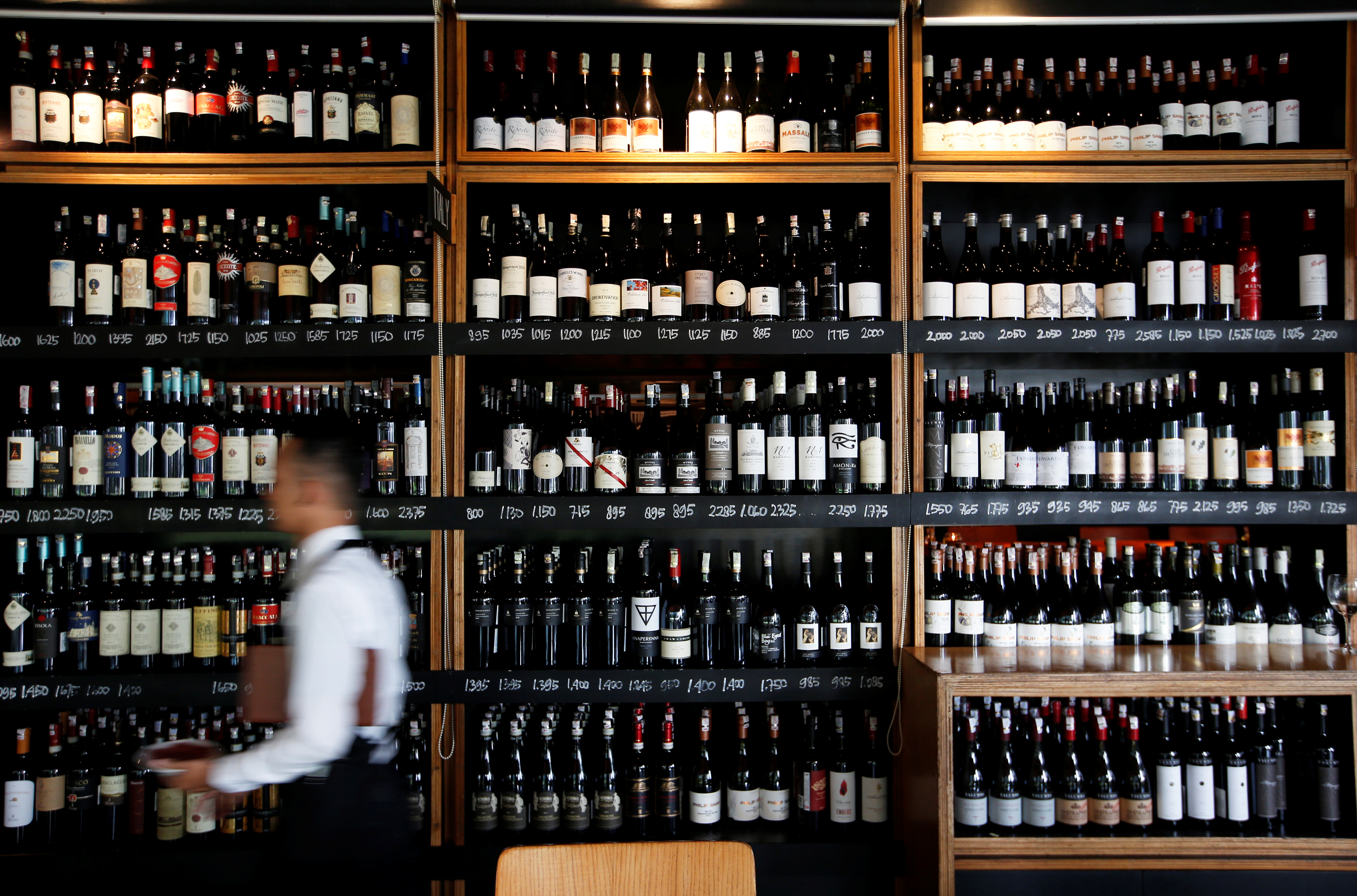 A server passes a wine rack at the Cork & Screw restaurant in Jakarta