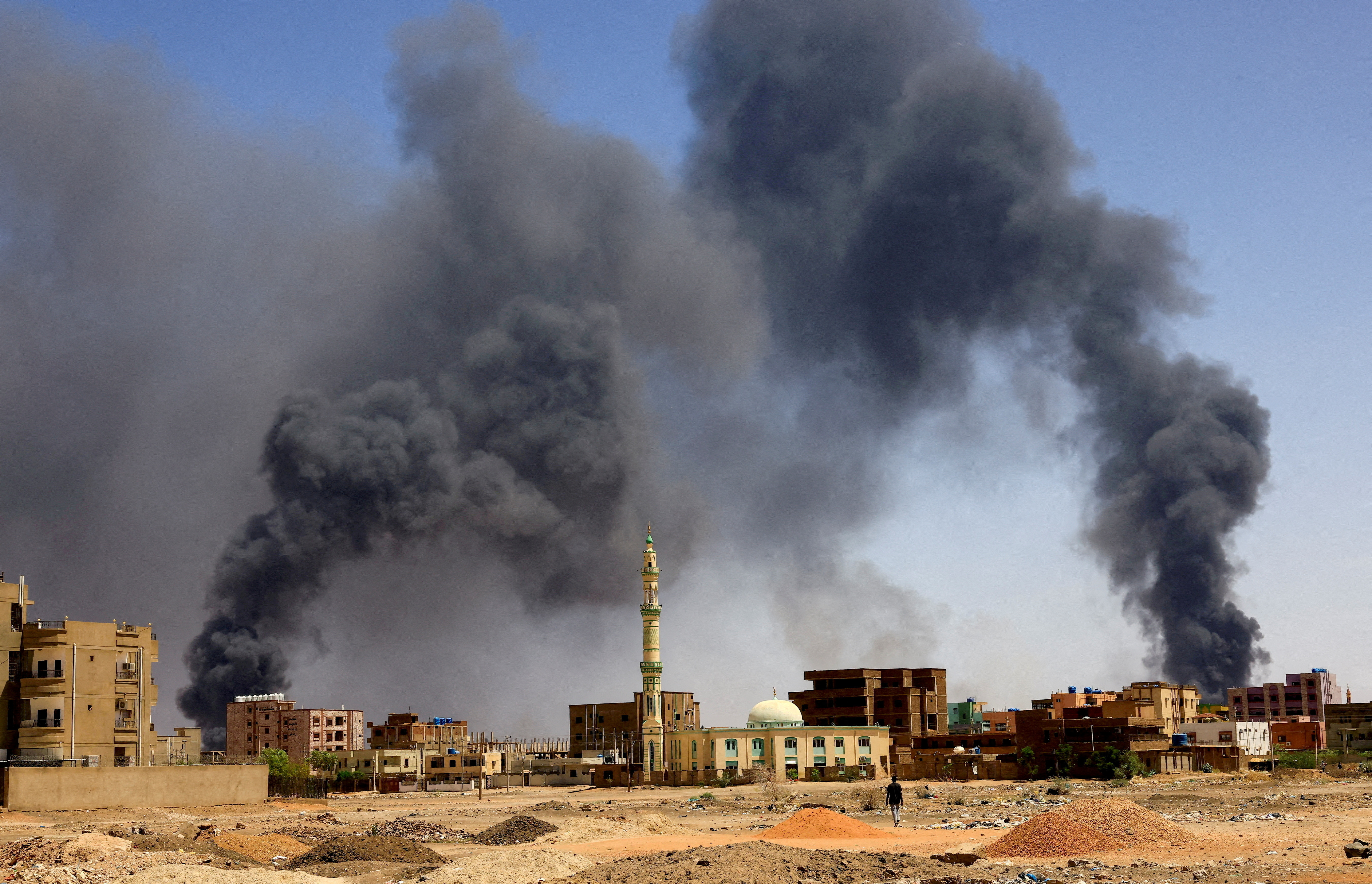 Un bărbat merge în timp ce fumul curge deasupra clădirilor după un bombardament aerian în Khartoum North