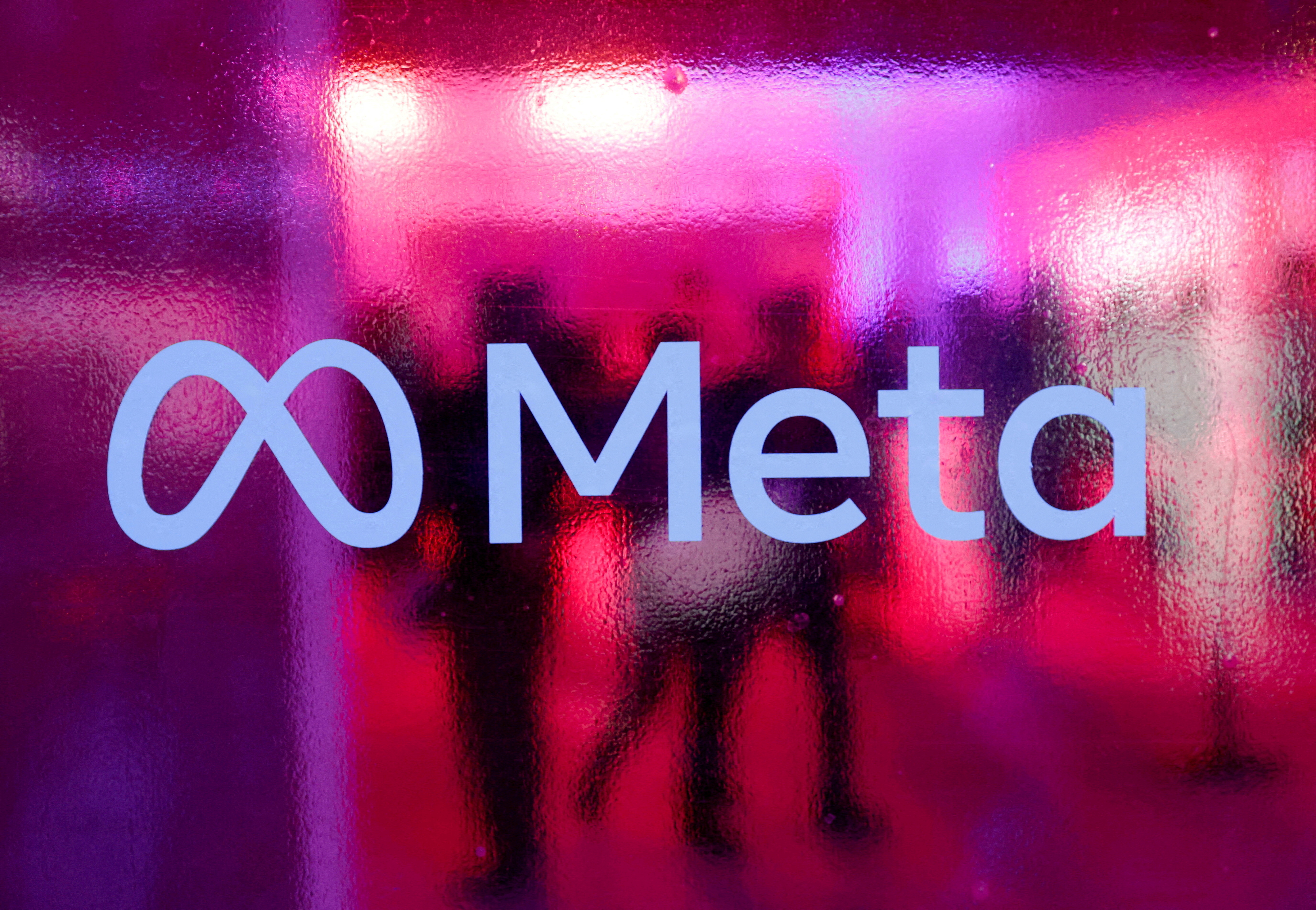 People walk behind a Meta Platforms logo during a conference in Mumbai,