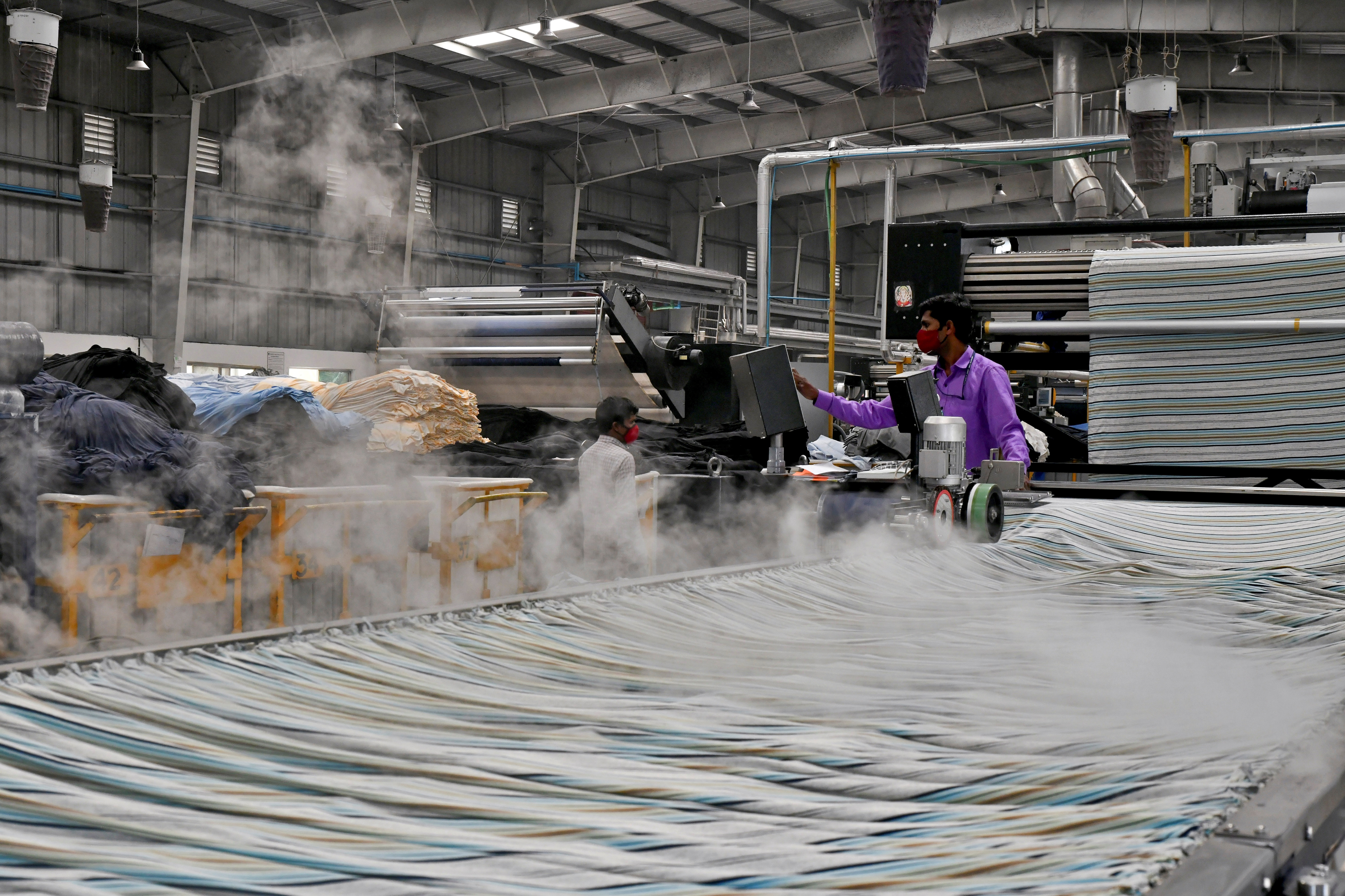 A worker mans a conveyor where dyed and washed garments are flattened, steamed and ironed at a textile factory of Texport Industries in Hindupur