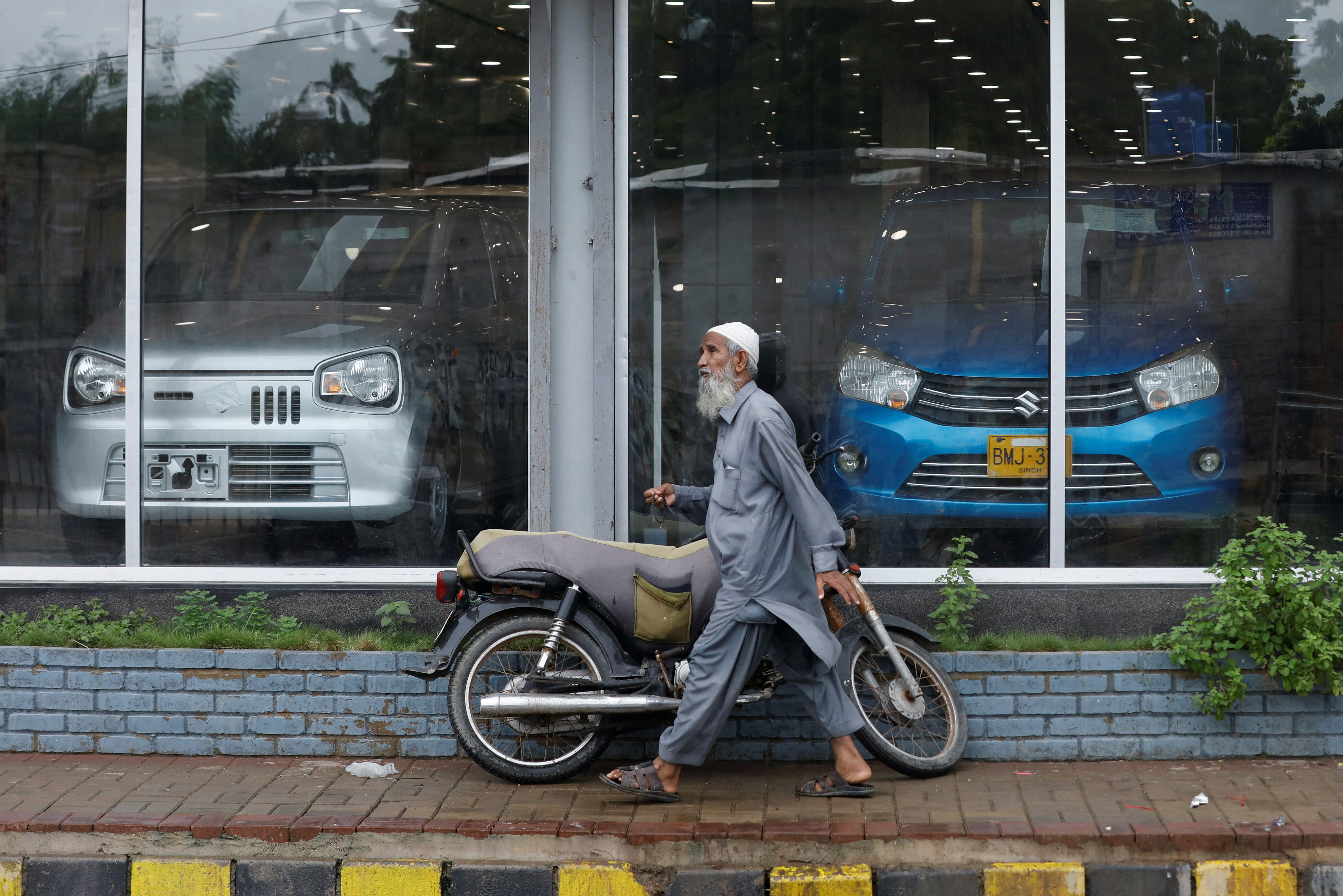 A man walks past a Suzuki outlet, displaying cars, in Karachi