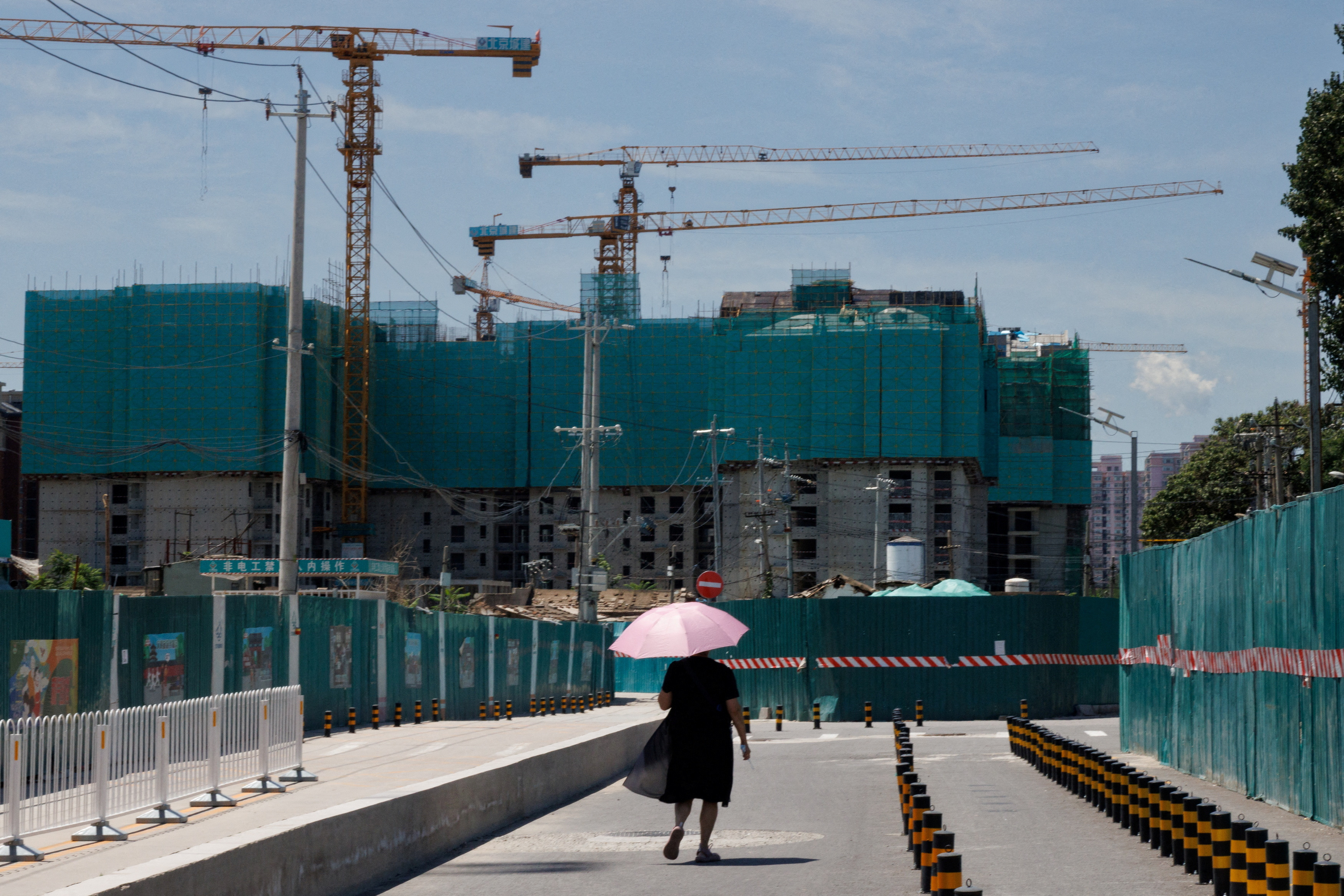A woman walks near a construction site of apartment buildings in Beijing