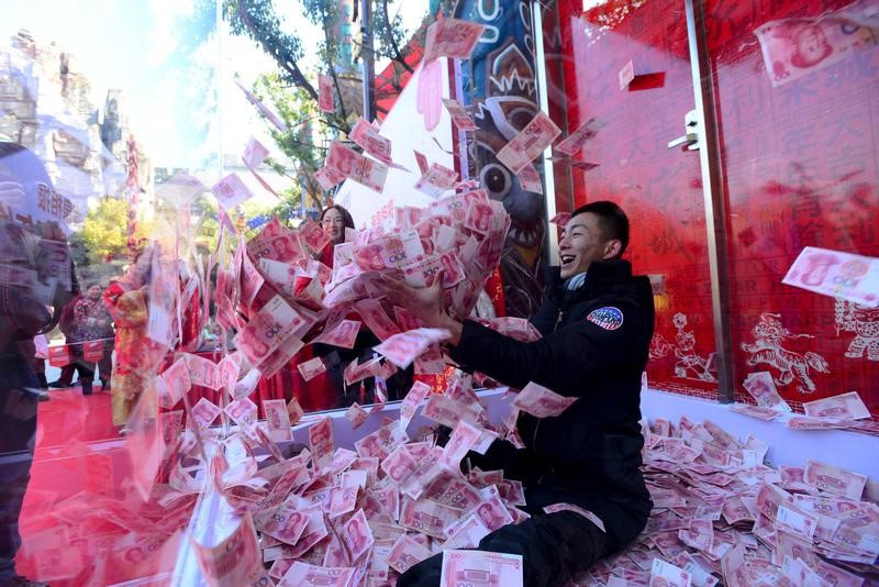 A man tries to snatch 100-yuan banknotes inside a glass cage during an event held to celebrate the upcoming Spring Festival, at a park in Hangzhou
