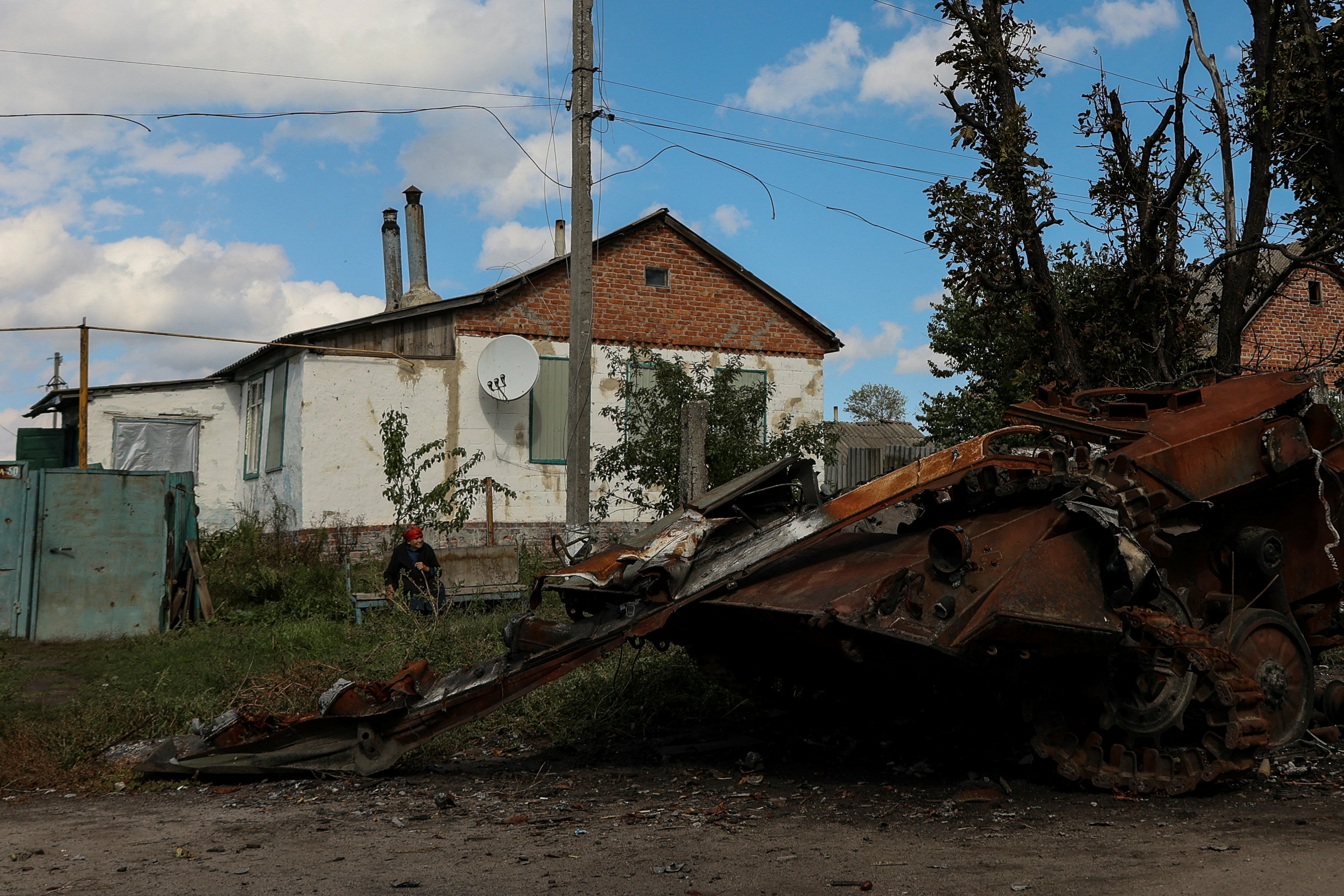 Woman looks at a destroyed Russian armoured fighting vehicle as she rests on a bench in the town of Balakliia