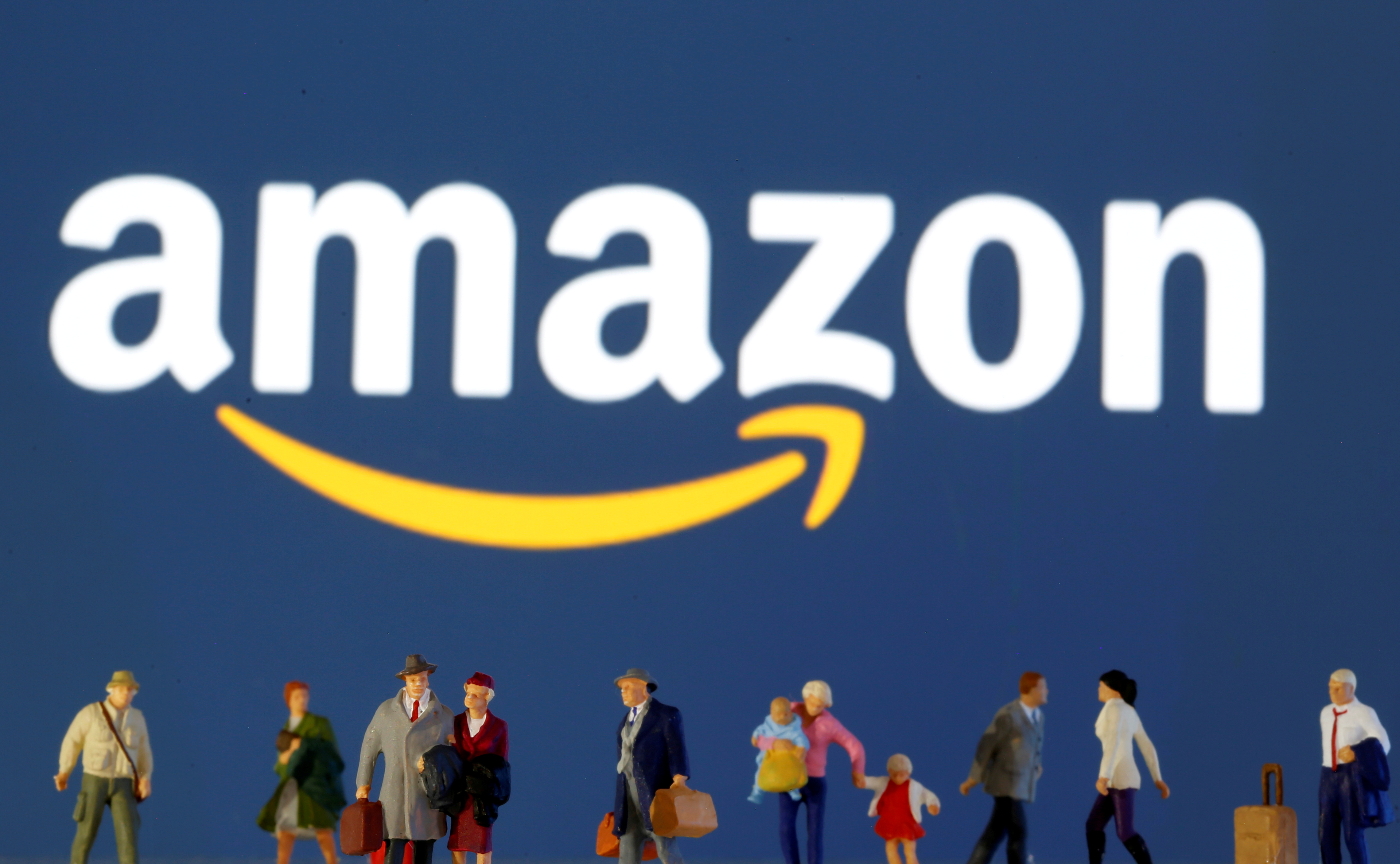 Small toy figures are seen in front of diplayed Amazon logo