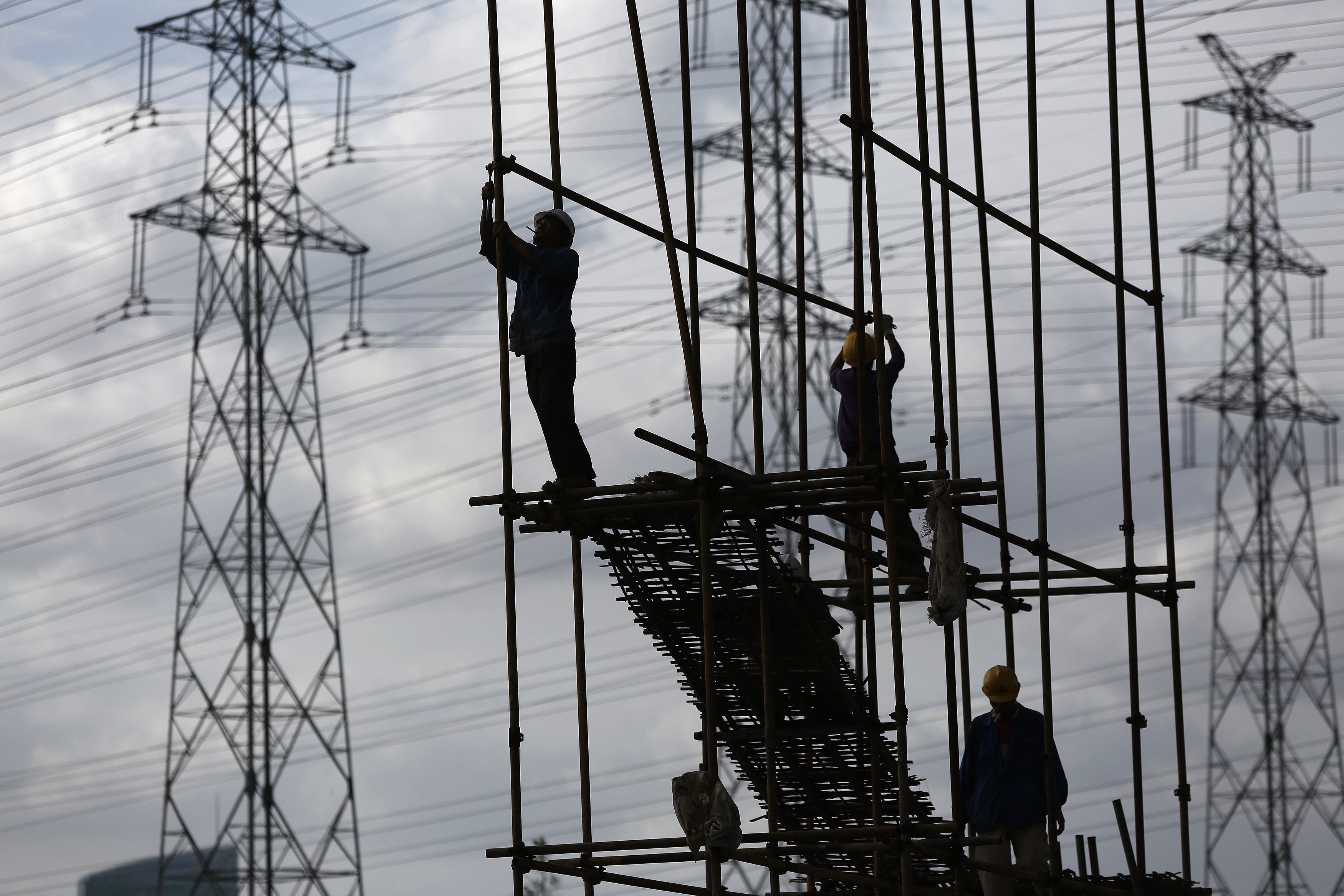 Construction workers stand on scaffolding in front of high voltage power lines in Shanghai