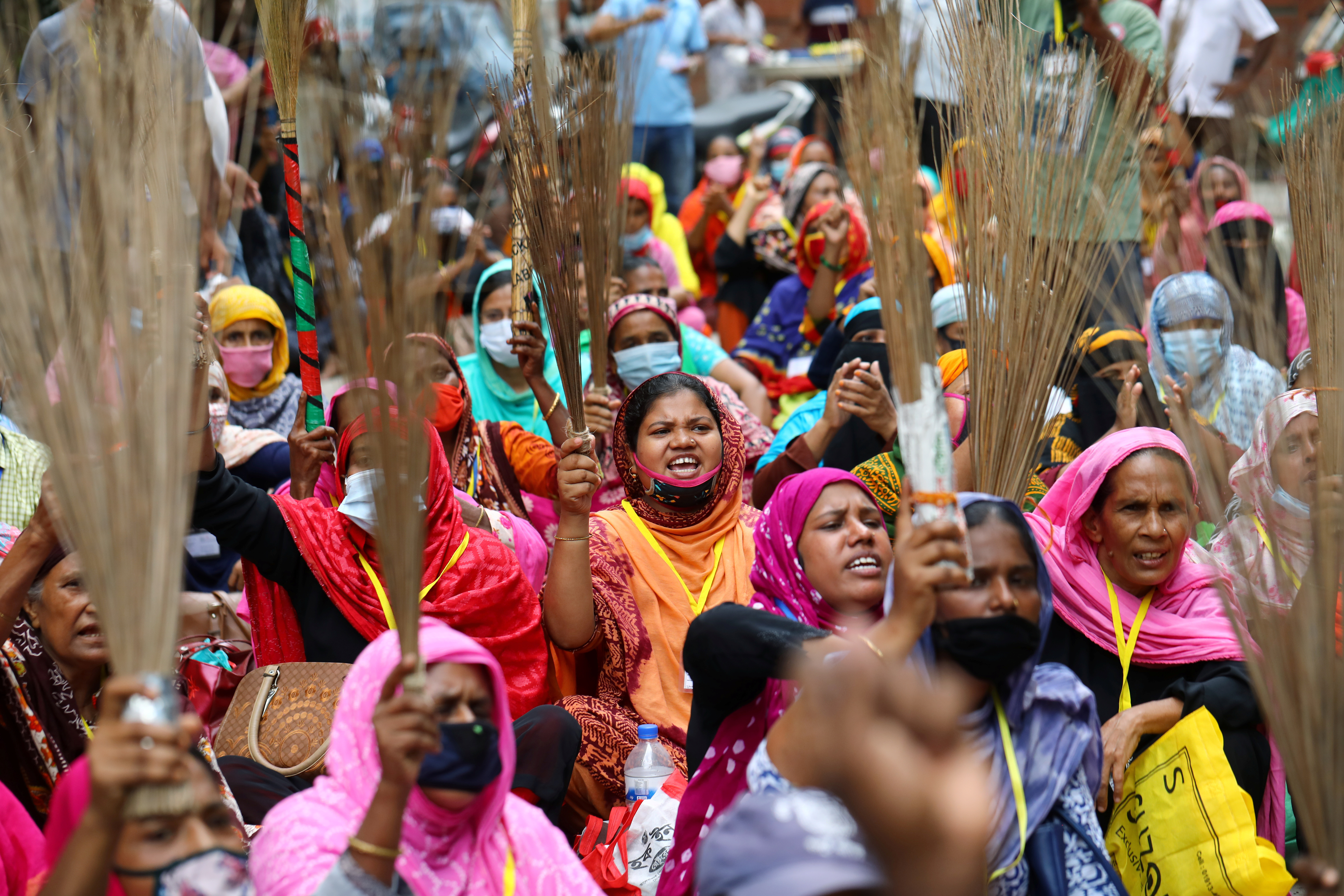 Garment workers shout slogans while holding brooms during a protest demanding their due wages in Dhaka