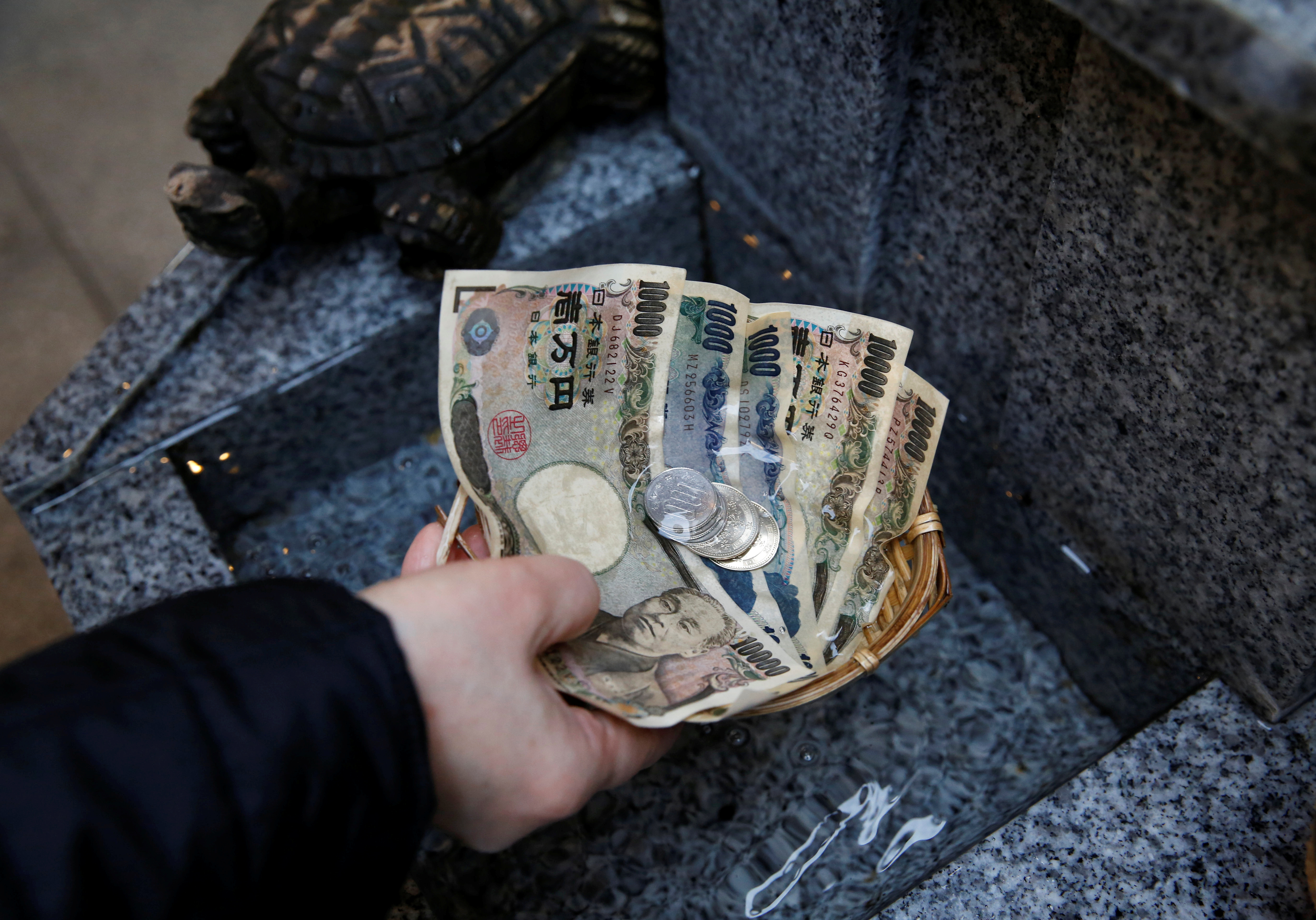 Visitor washes Japanese yen banknotes and coins in water to pray for prosperity at Koami shrine in Tokyo's Nihonbashi business district