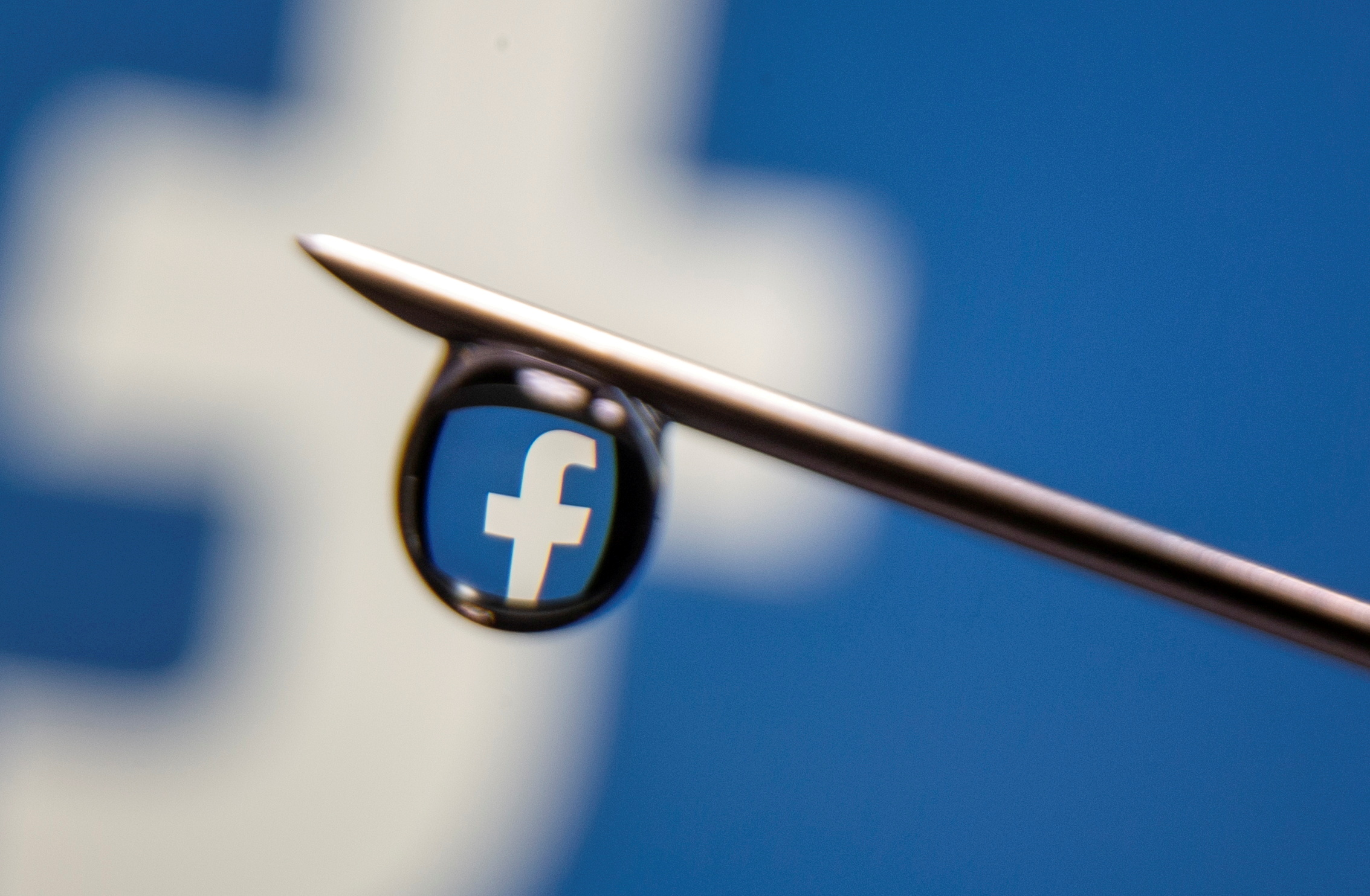 Facebook logo is reflected in a drop on a syringe needle in this illustration photo