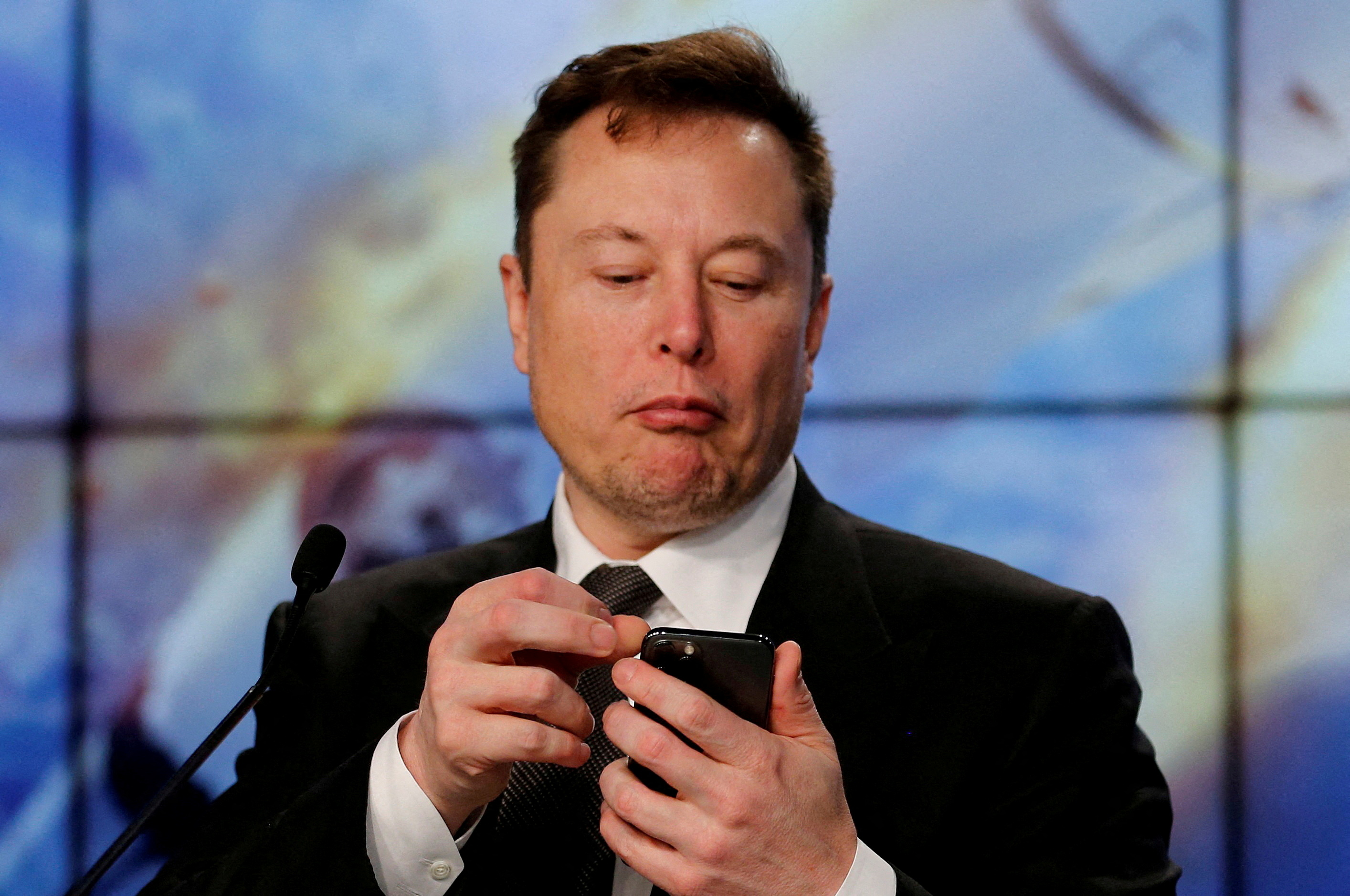 Elon Musk looks at his mobile phone during a post-launch news conference to discuss the  SpaceX Crew Dragon astronaut capsule in-flight abort test at the Kennedy Space Center