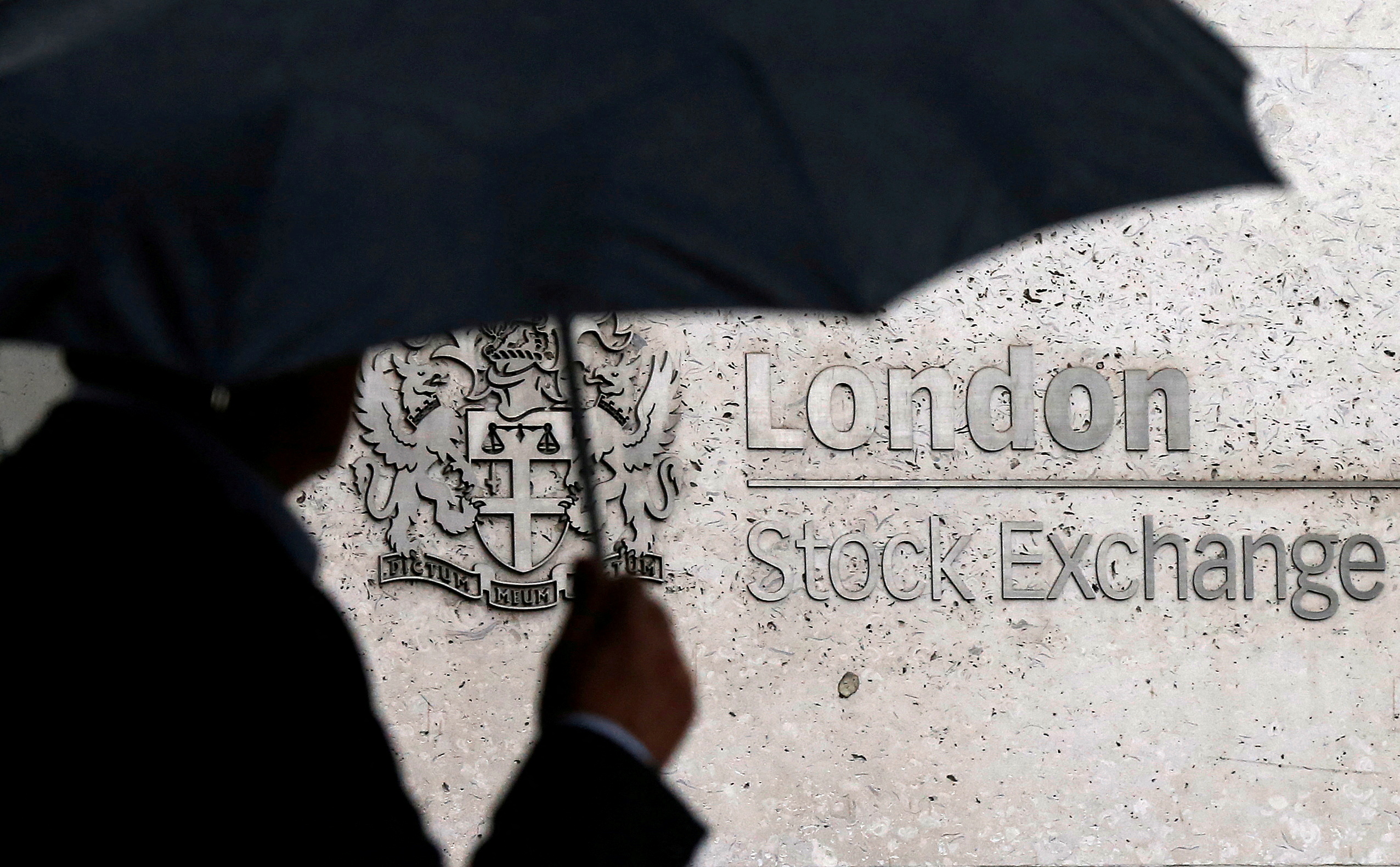 A man shelters under an umbrella as he walks past the London Stock Exchange