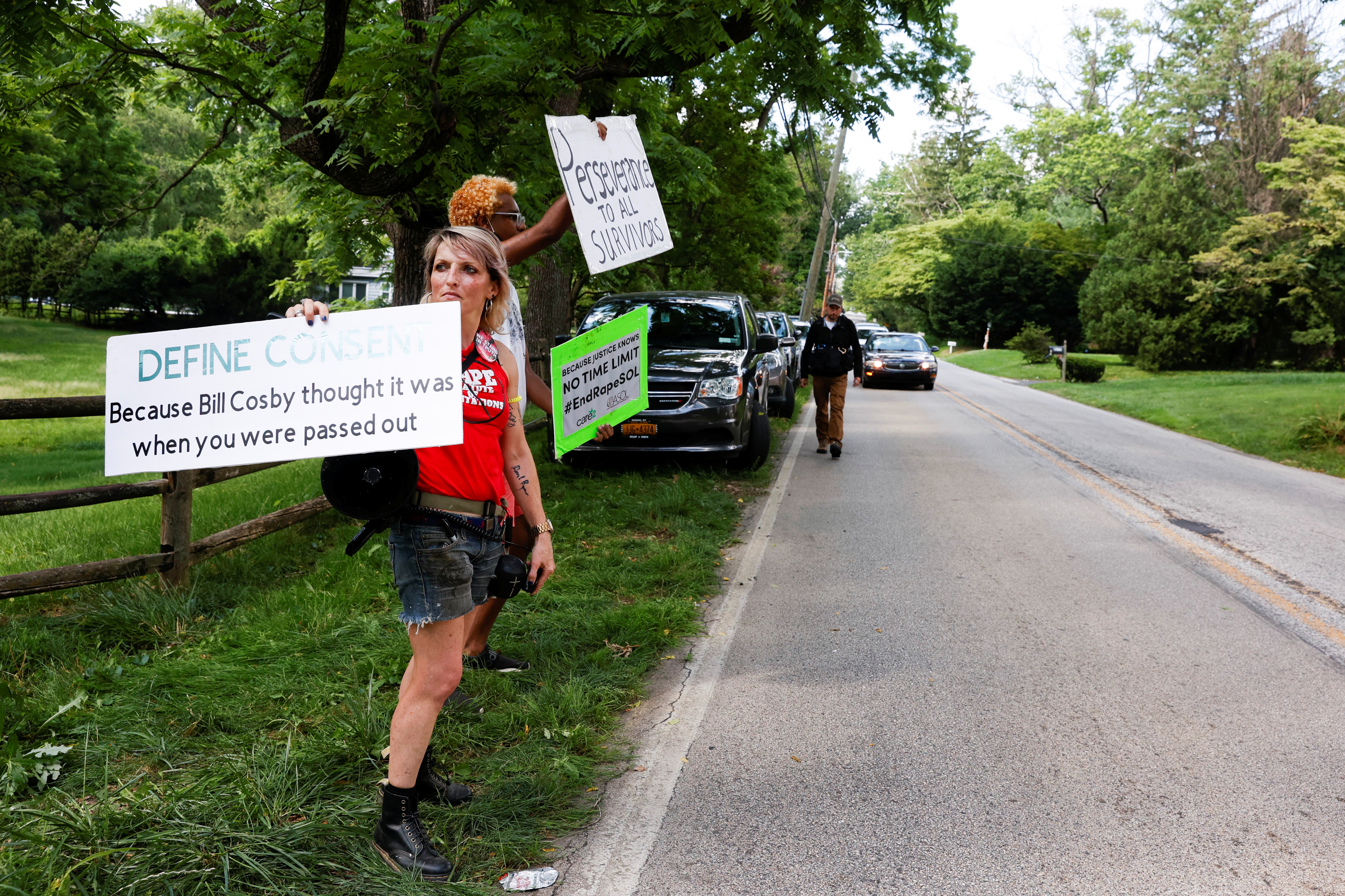 People hold placards on the road outside Bill Cosby's house after Pennsylvania's highest court overturned Cosby's sexual assault conviction and ordered him released from prison immediately, in Elkins Park