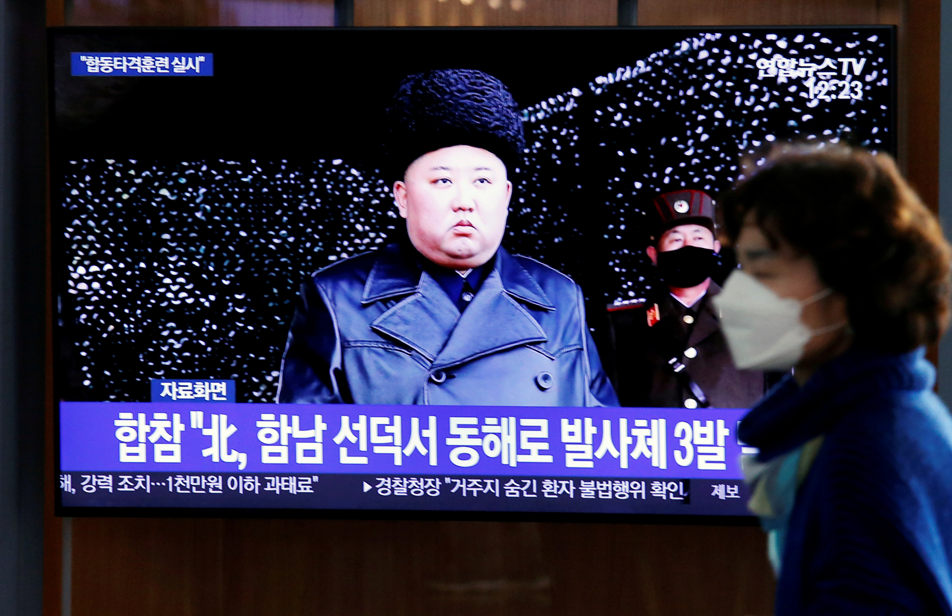 A woman walks past a TV broadcasting file footage for a news report on North Korea firing an unidentified projectile, in Seoul