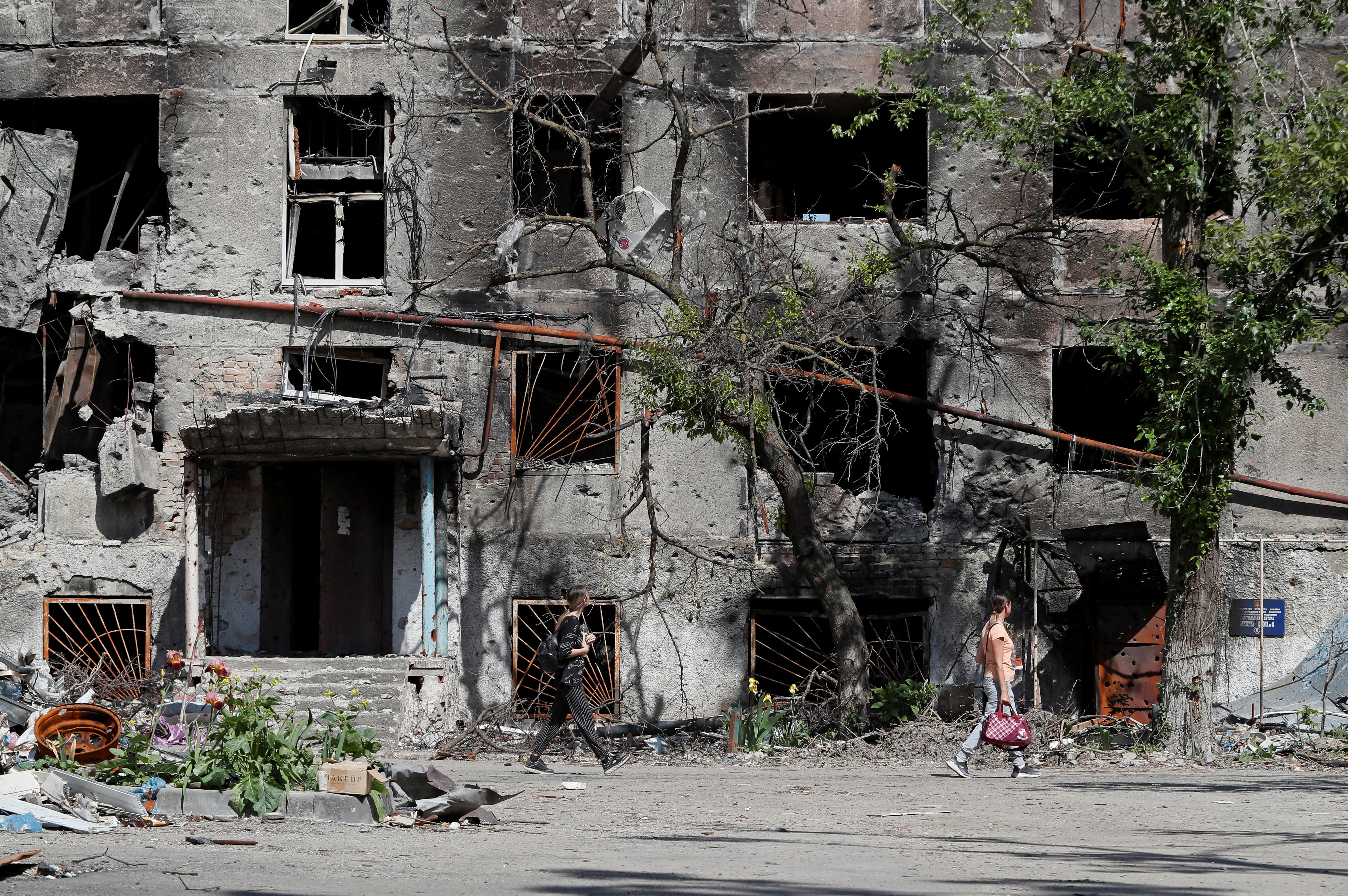 FILE PHOTO: People walk past a heavily damaged residential building in Mariupol