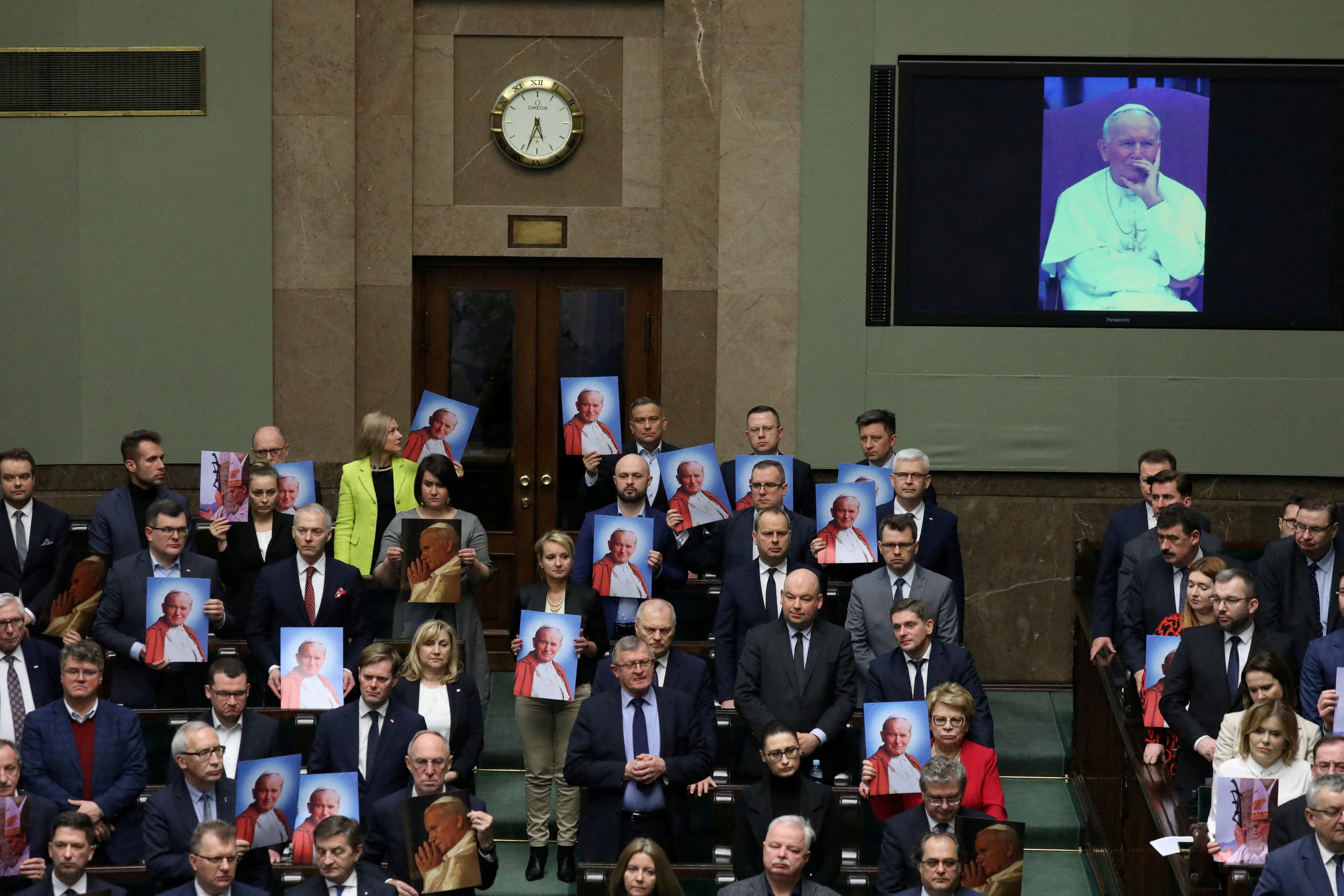 Lawmakers hold images of Pope John Paul II during debate about resolution on defending his name, in Warsaw