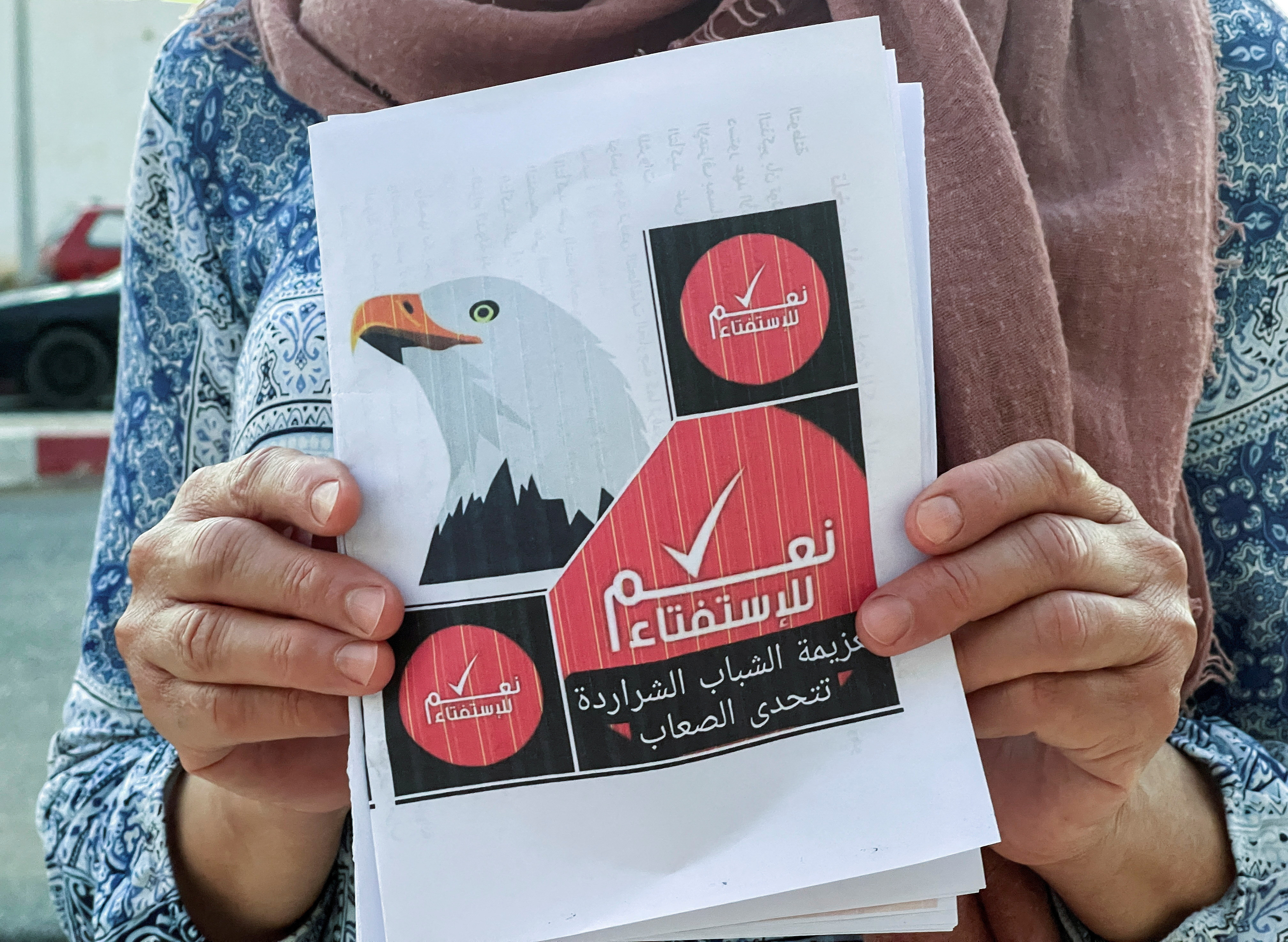 A volunteer displays a campaign flyer for an upcoming referendum on a new constitution, in Kairouan