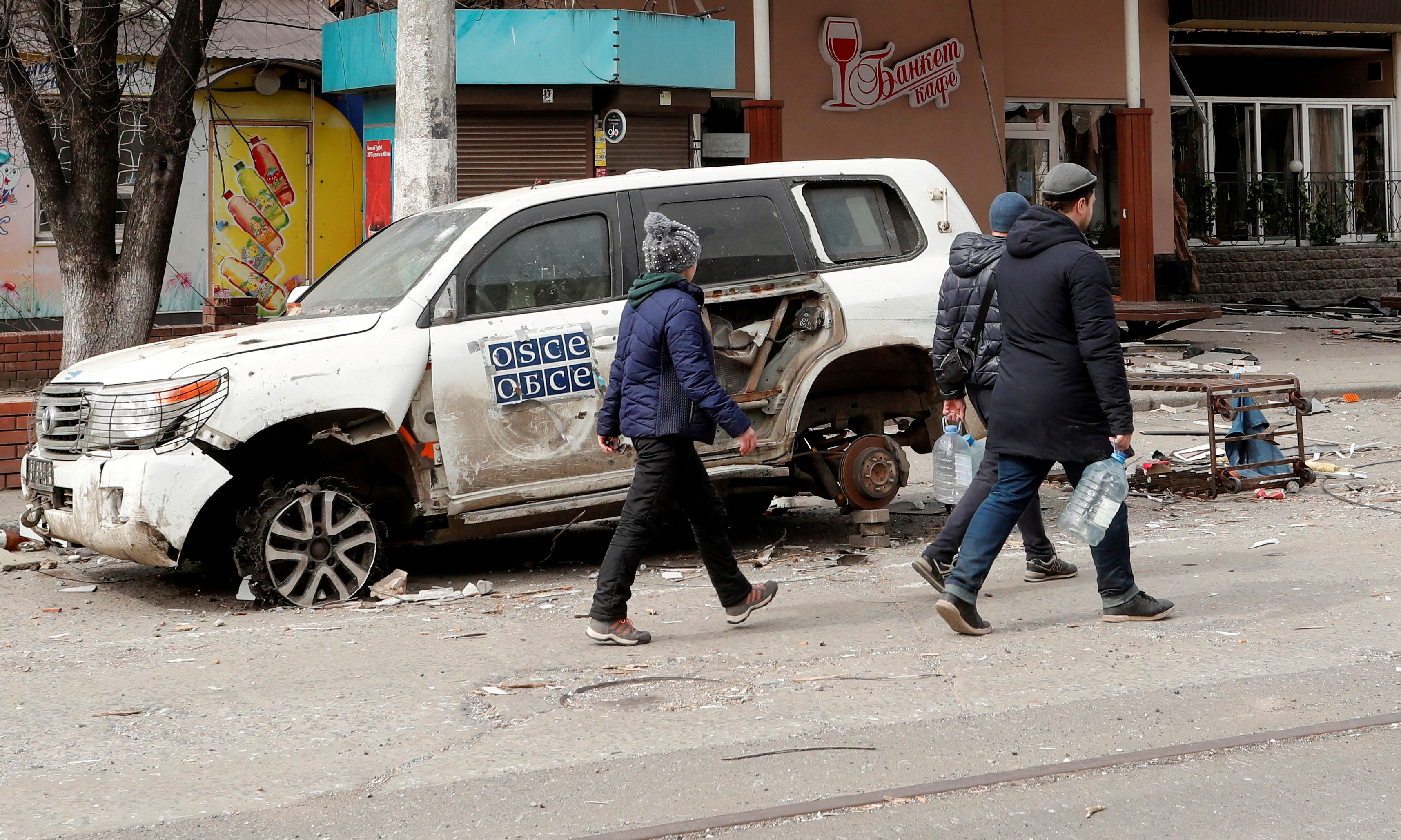 People walk past a damaged OSCE car in Mariupol