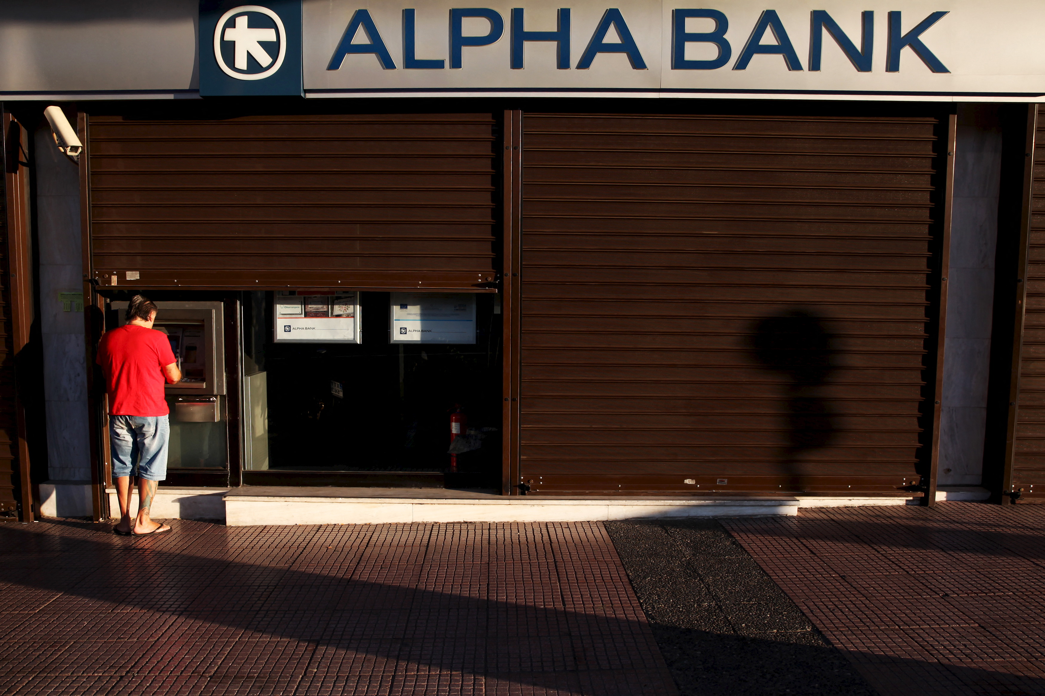 A man withdraws money at an Alpha Bank branch ATM in central Athens