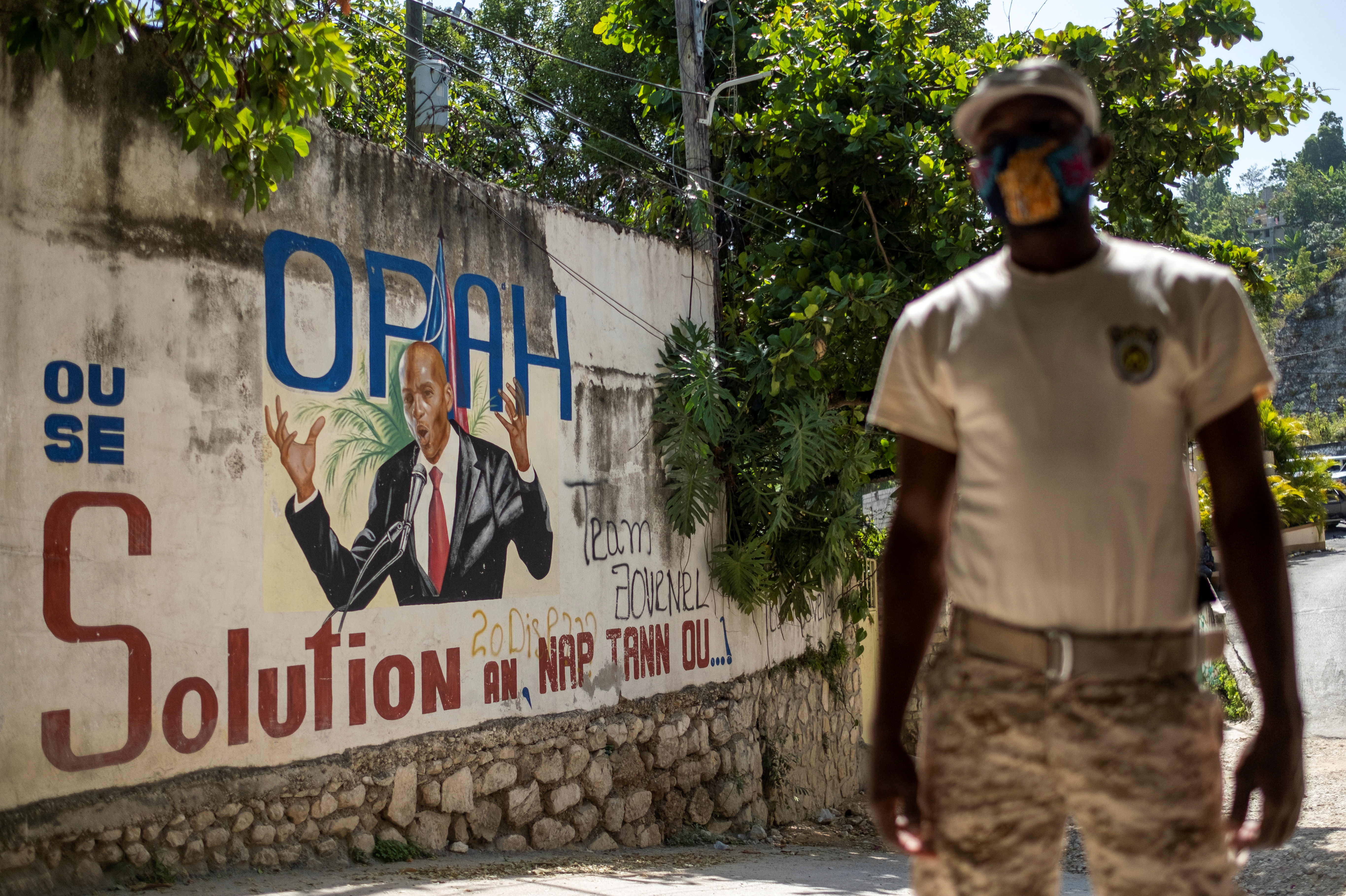 A Haitian police officer stands near a mural featuring President Jovenel Moise in Port-au-Prince
