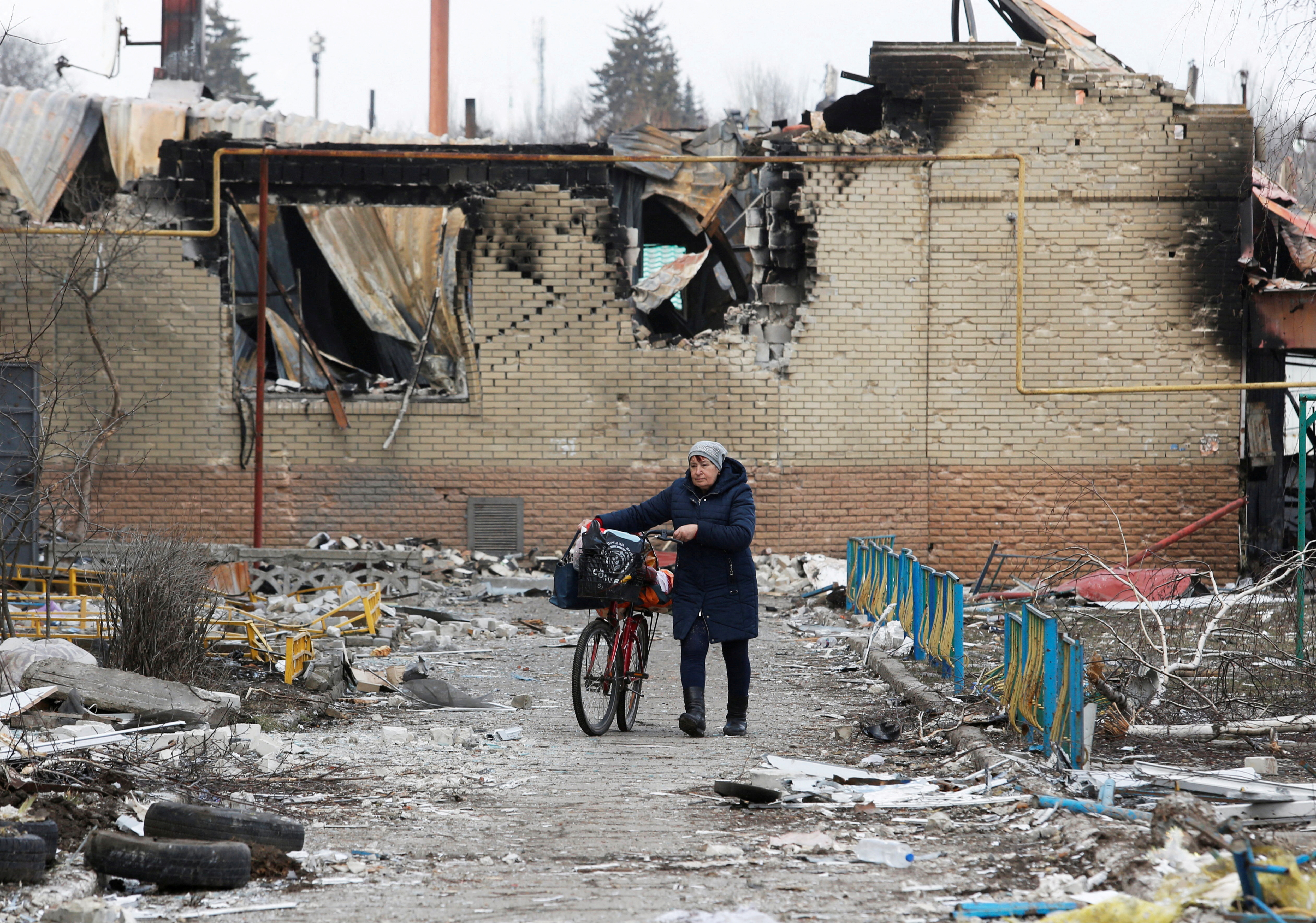 A woman walks with a bicycle next to a damaged building in Volnovakha