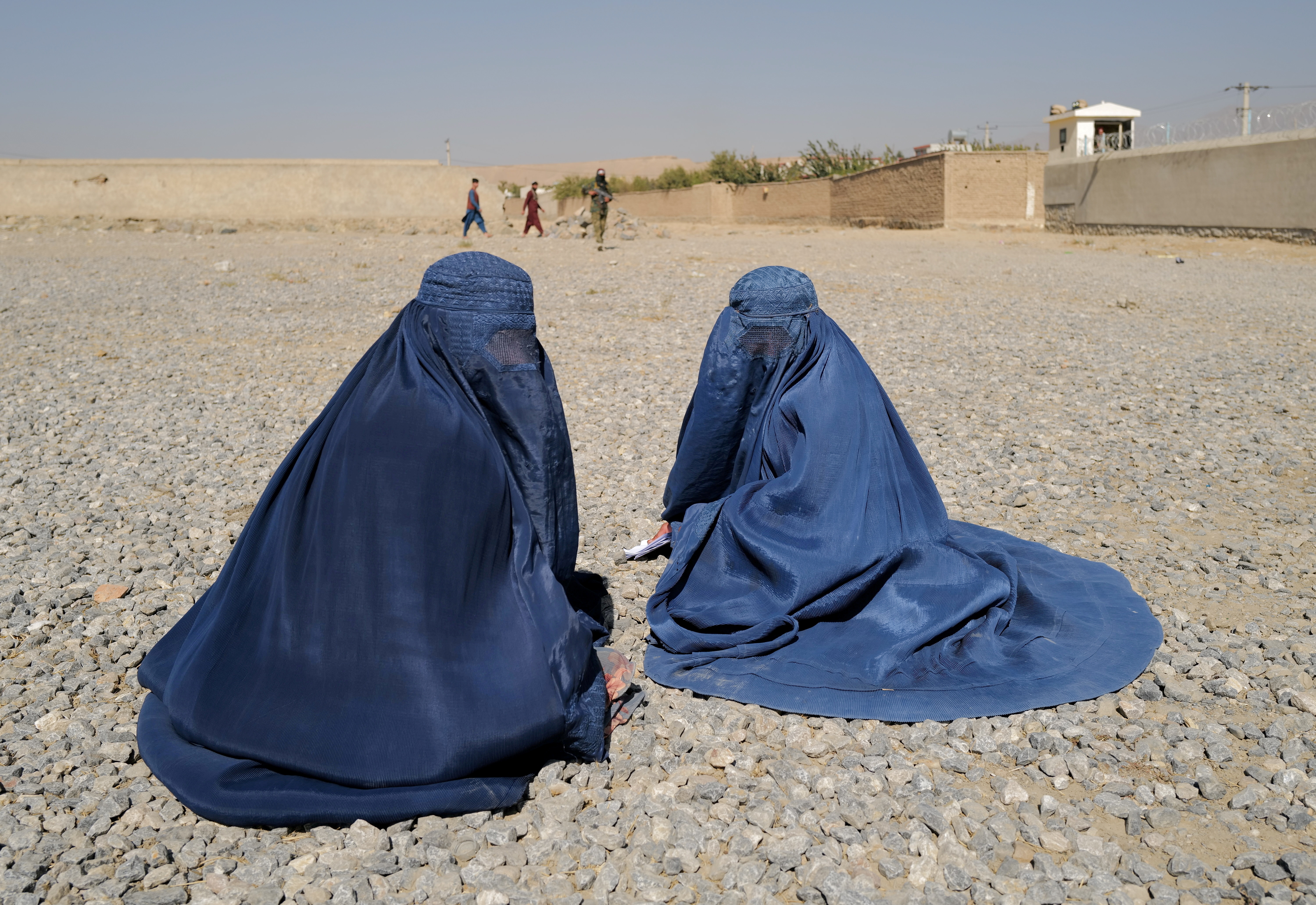 Displaced Afghan women wait to receive aid supply from UNHCR agency outside the distribution center on the outskirts of Kabul