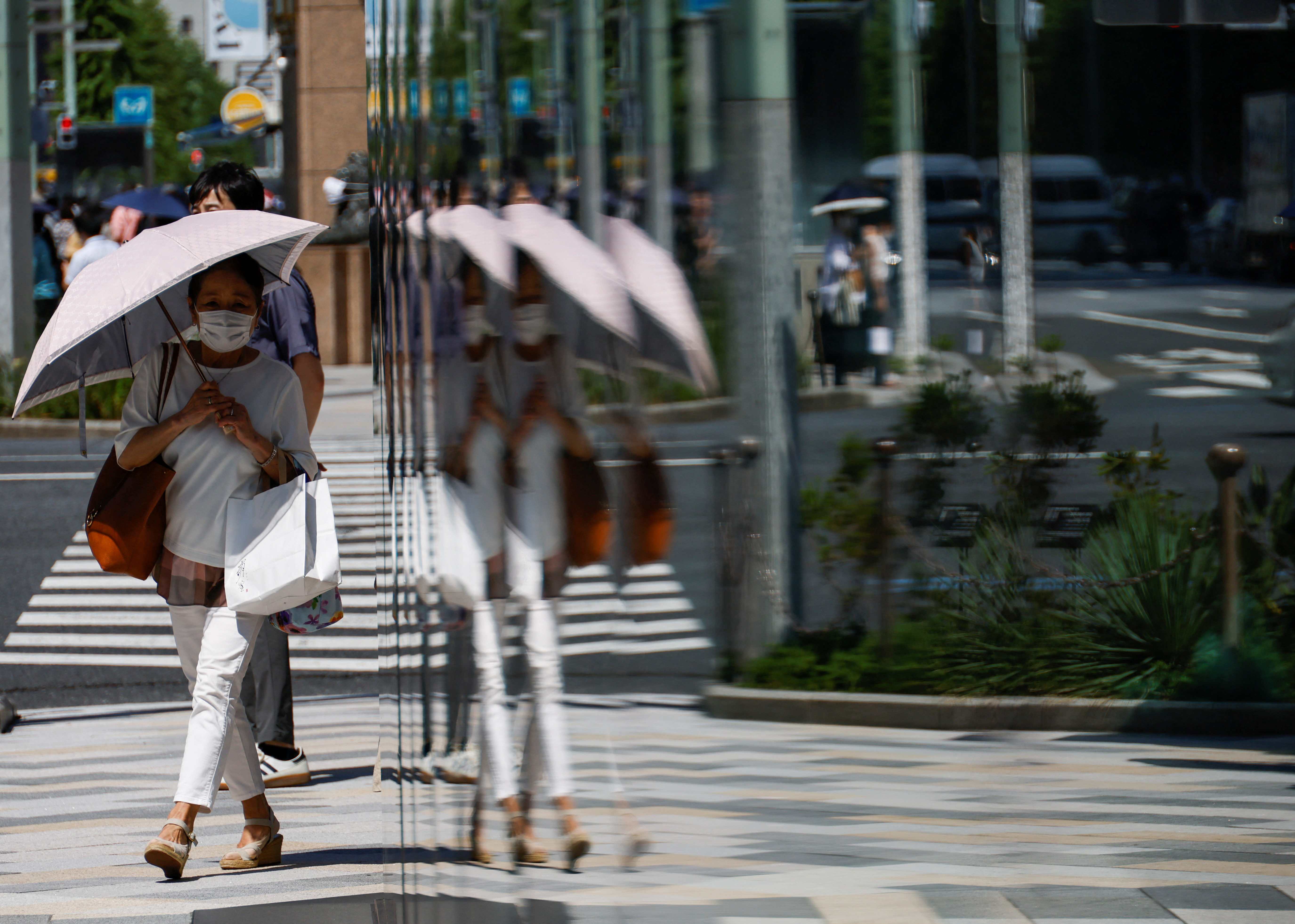 A woman holding an umbrella is reflected on a window while walking along a street in Tokyo
