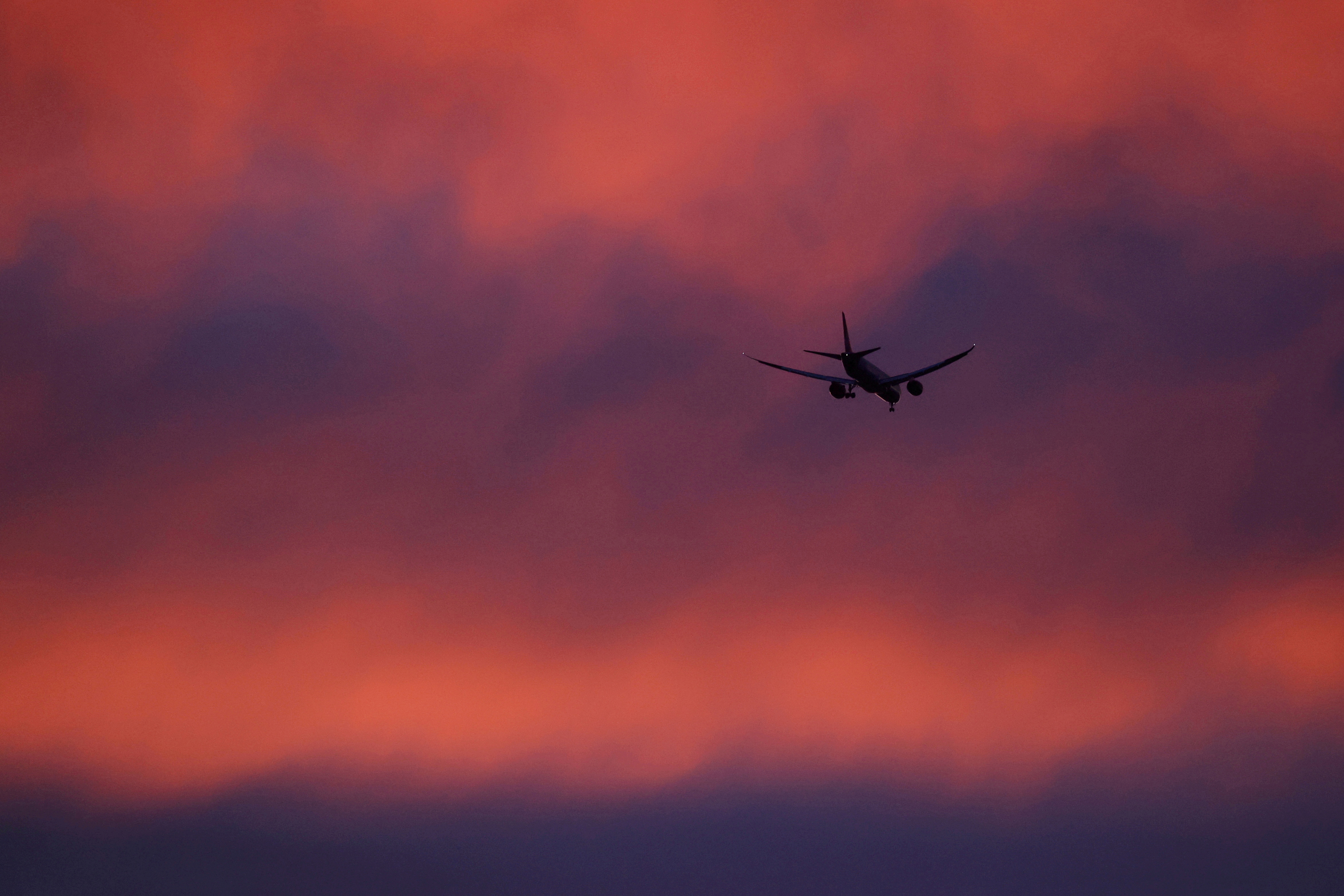 A plane flies in a red sky above London