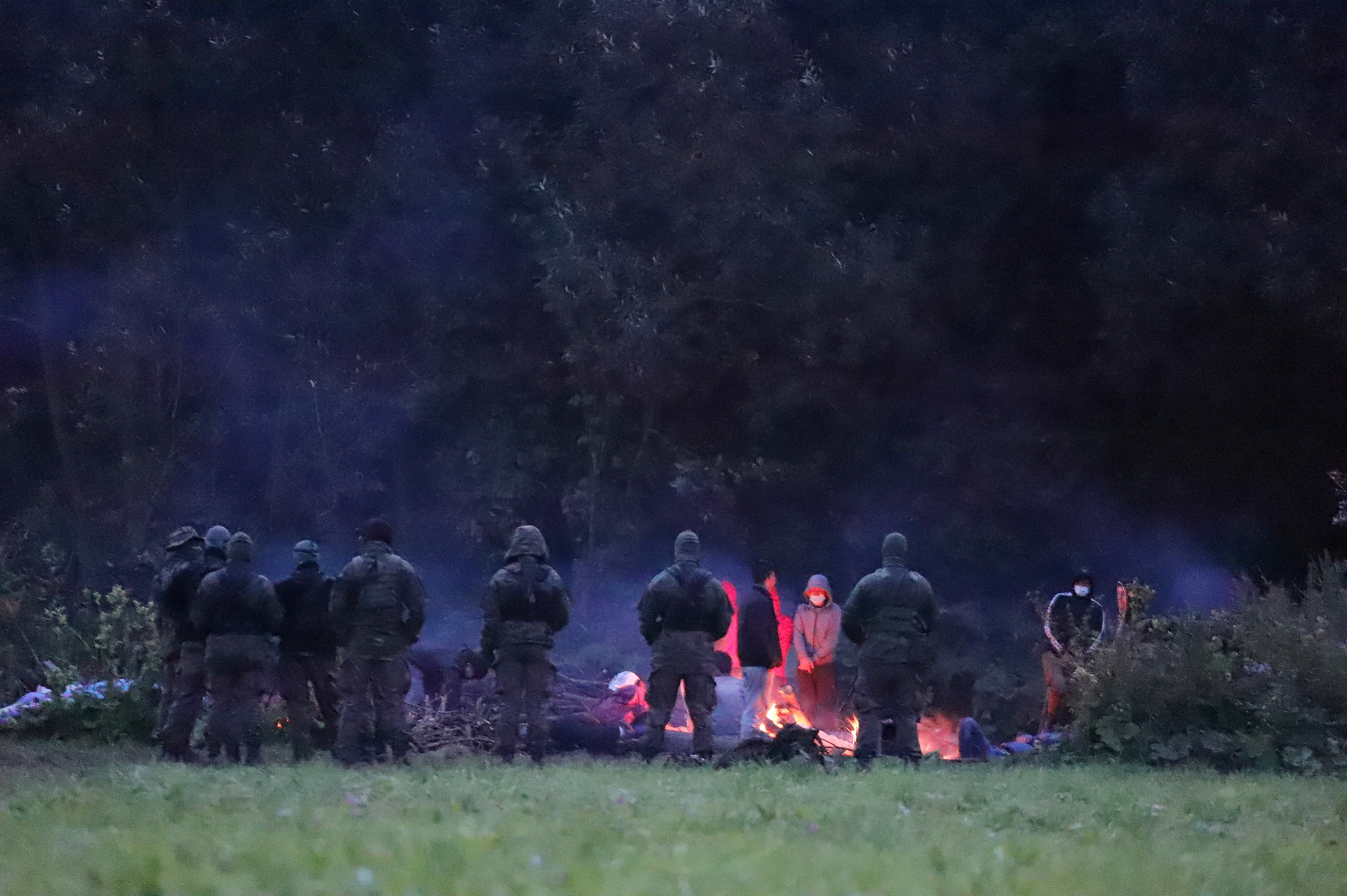 Polish border patrol officers guard a group of migrants who attempted to cross the border between Belarus and Poland near the village of Usnarz Gorny