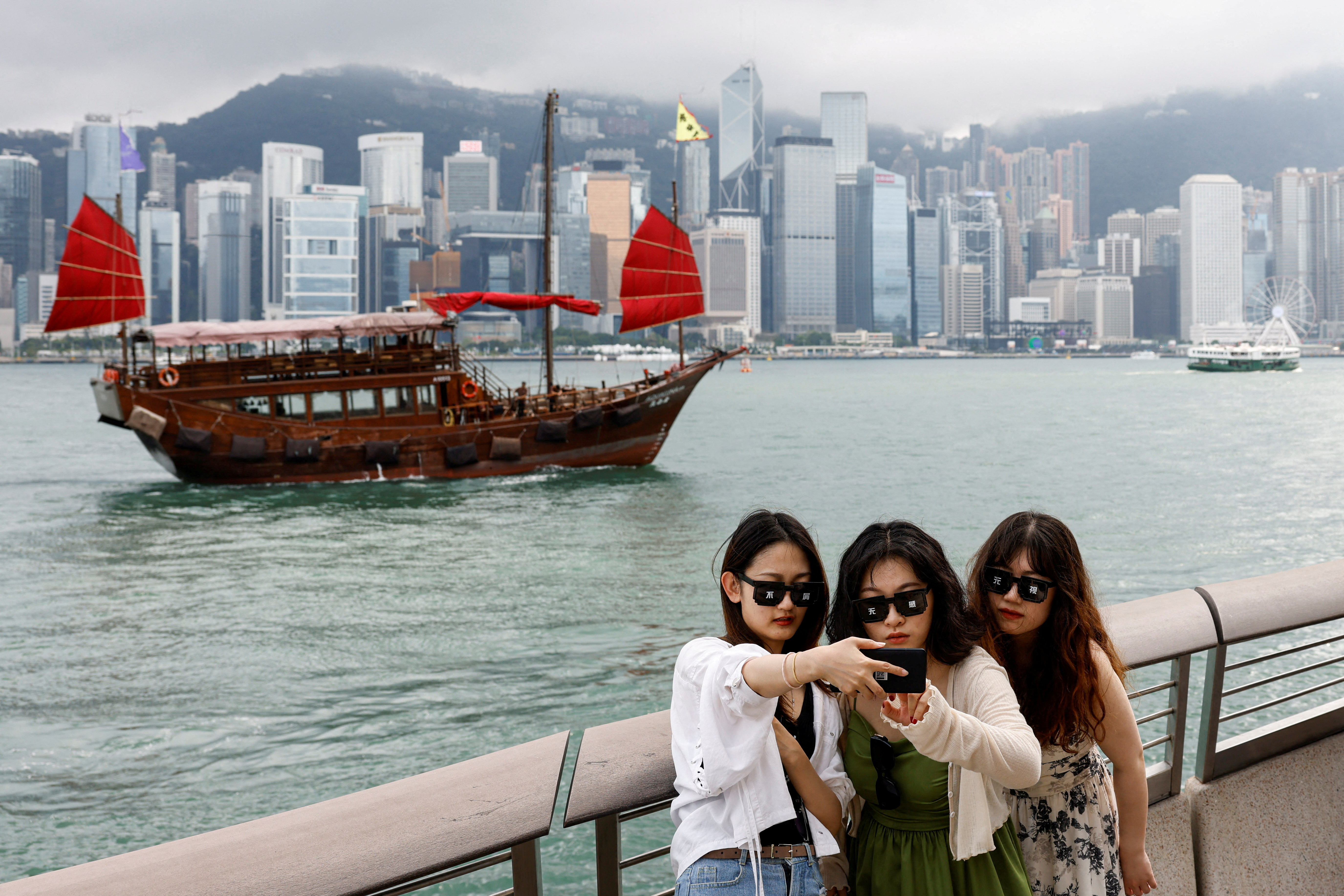Tourists take photos in front of Victoria Harbour, in Tsim Sha Tsui, in Hong Kong
