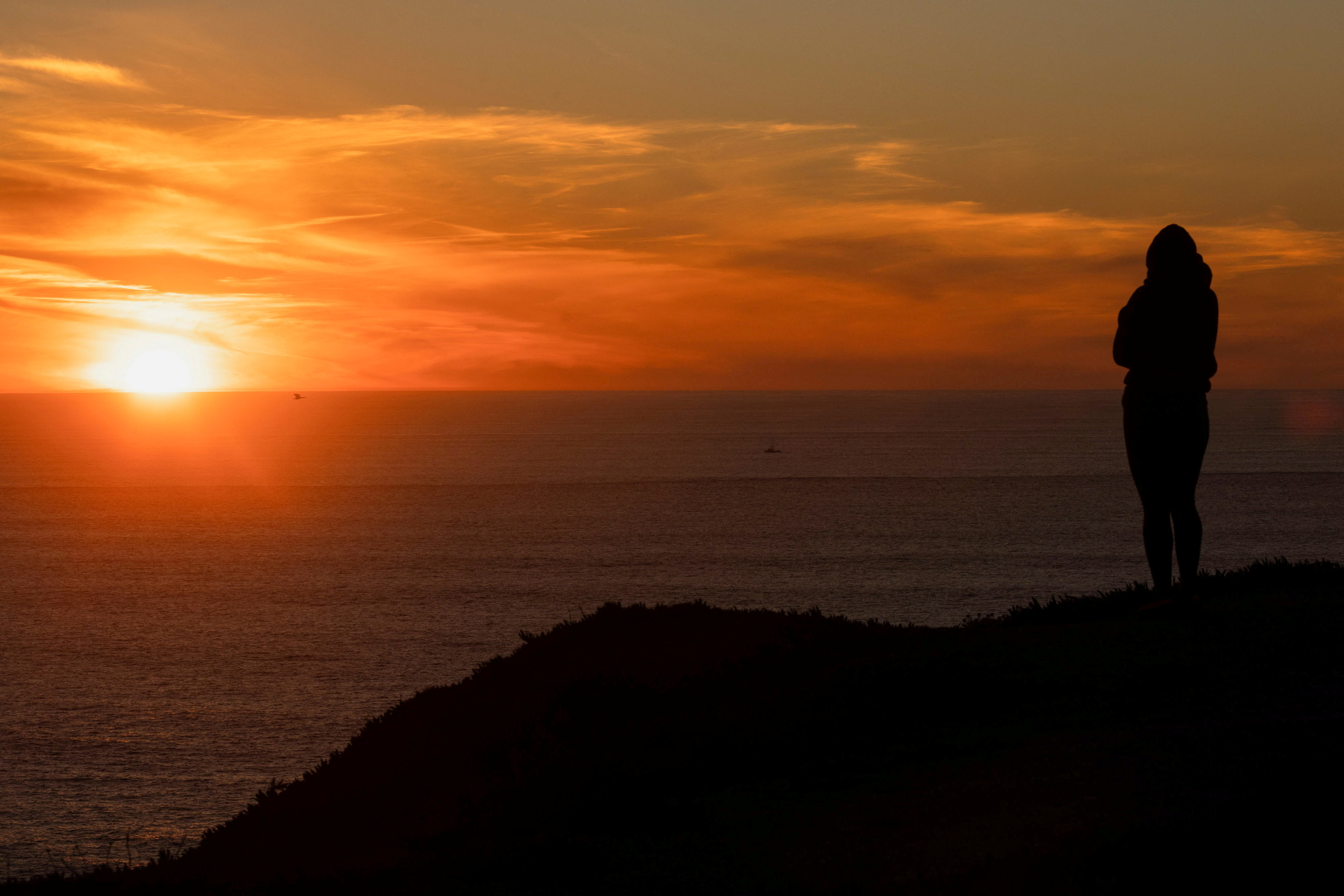 A woman watches the sunset over the Pacific Ocean along Highway 1 near Half Moon Bay