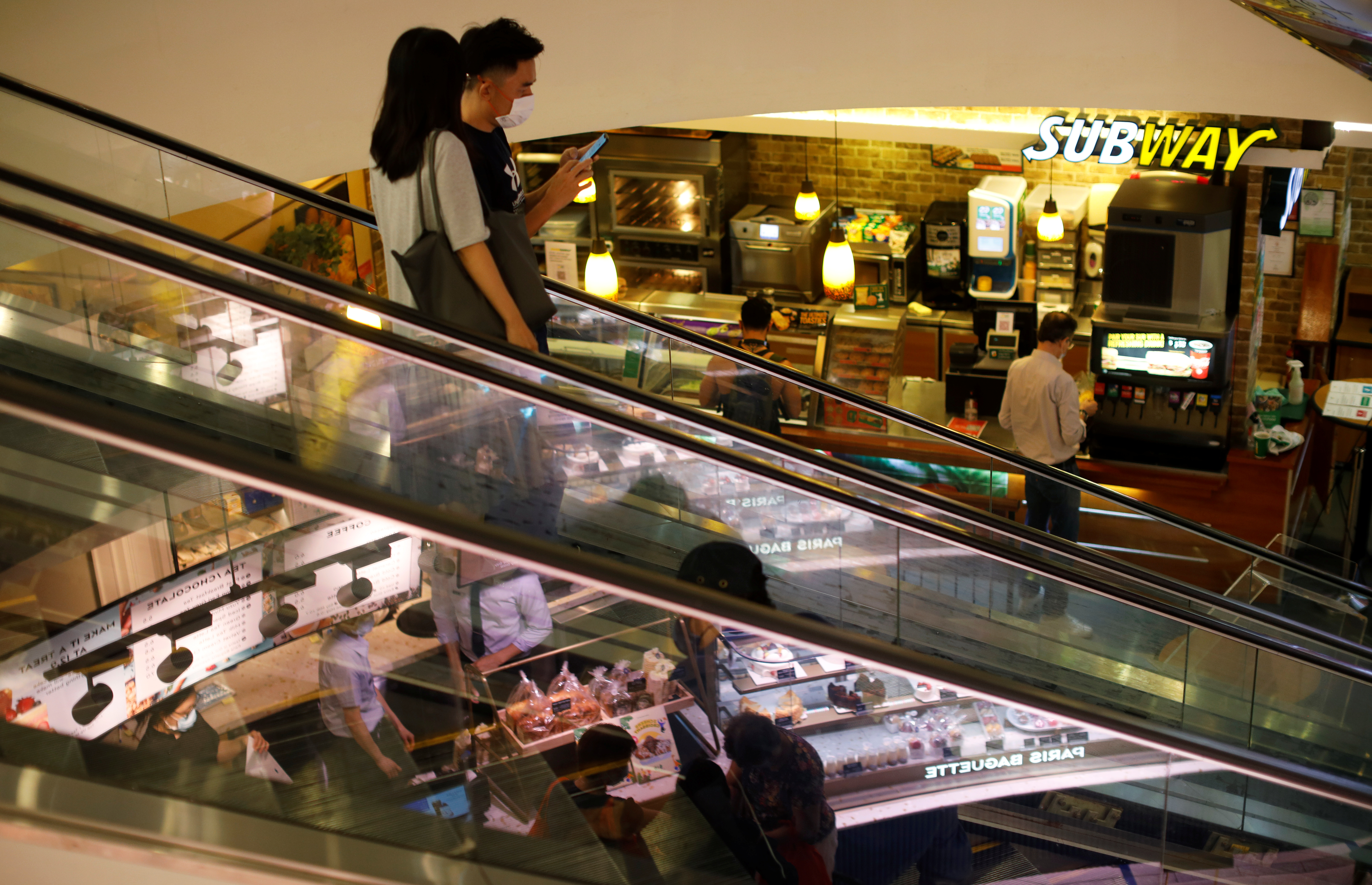 People wearing protective face masks ride an escalator at a shopping mall in Singapore