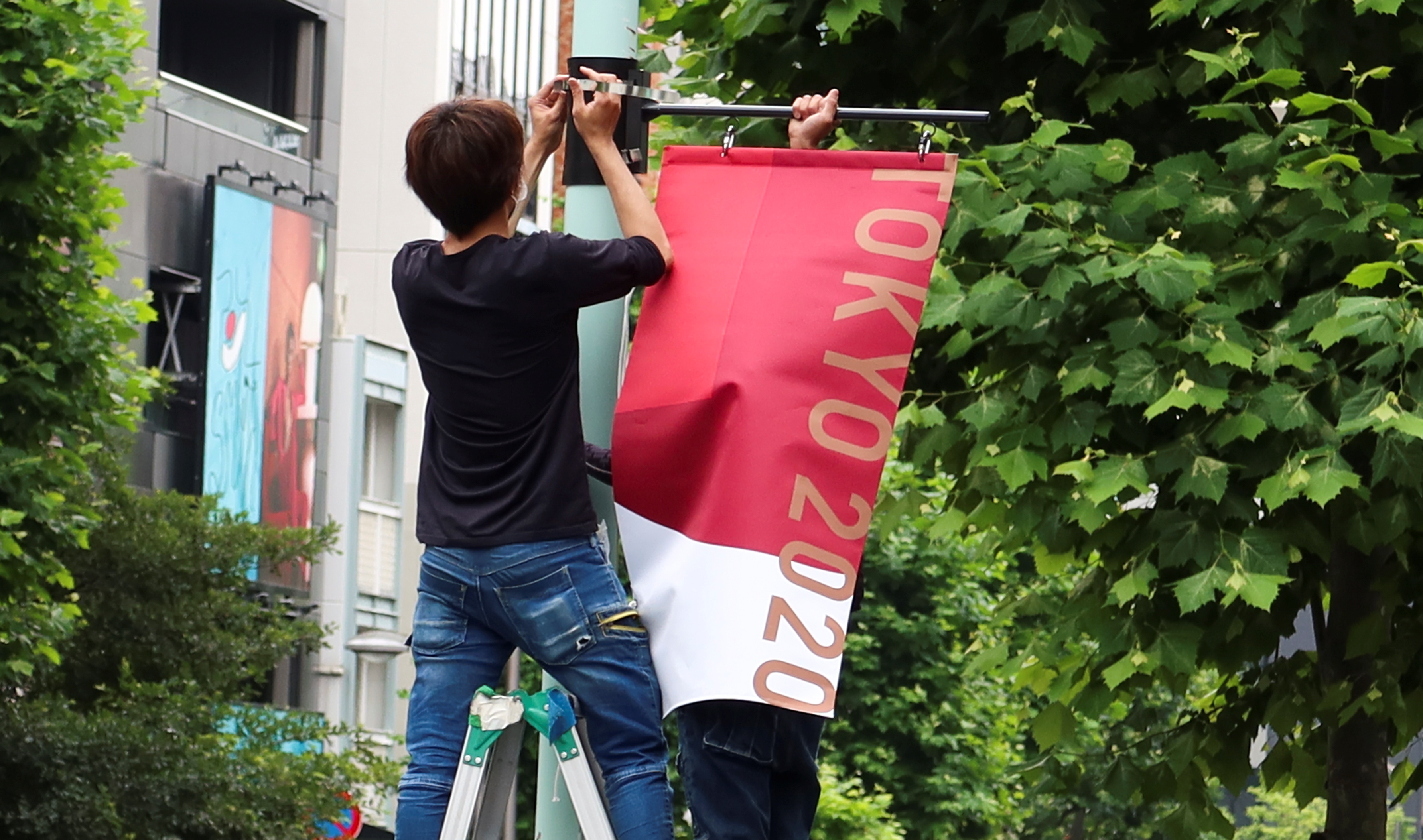 Workers attach the Tokyo 2020 Olympic Games banner on a lamp post in Tokyo