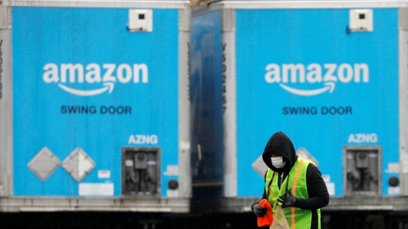 A worker in a face mask walks by trucks parked at an Amazon facility as the global coronavirus outbreak continued in Bethpage on Long Island in New York