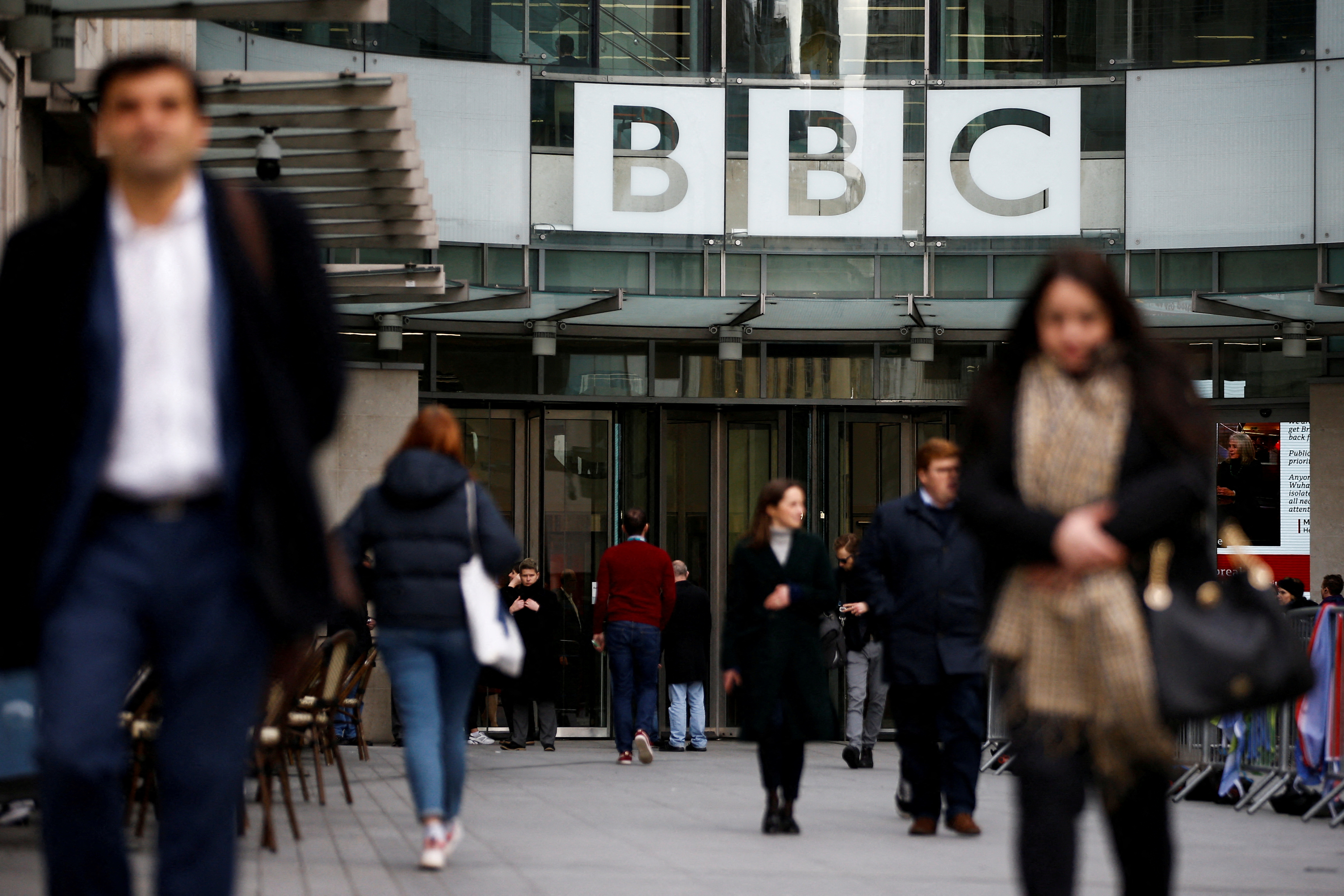 Pedestrians walk past a BBC logo at Broadcasting House, as the corporation announced it will cut around 450 jobs from its news division, in London