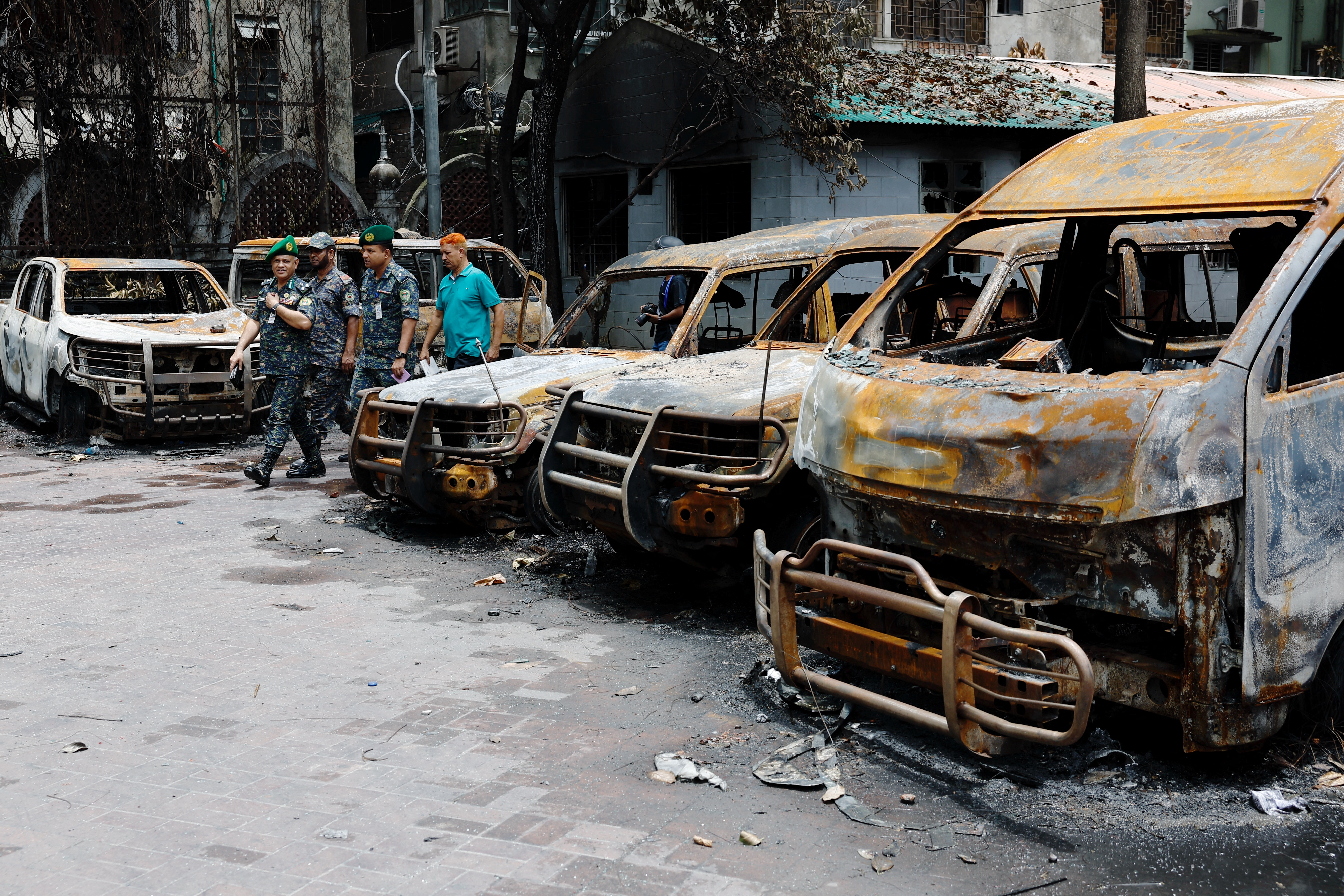 Security personnel walk past damaged vehicles of a government owned organization, that were set afire by a mob during clashes after violence erupted following protests by students against government job quotas, in Dhaka