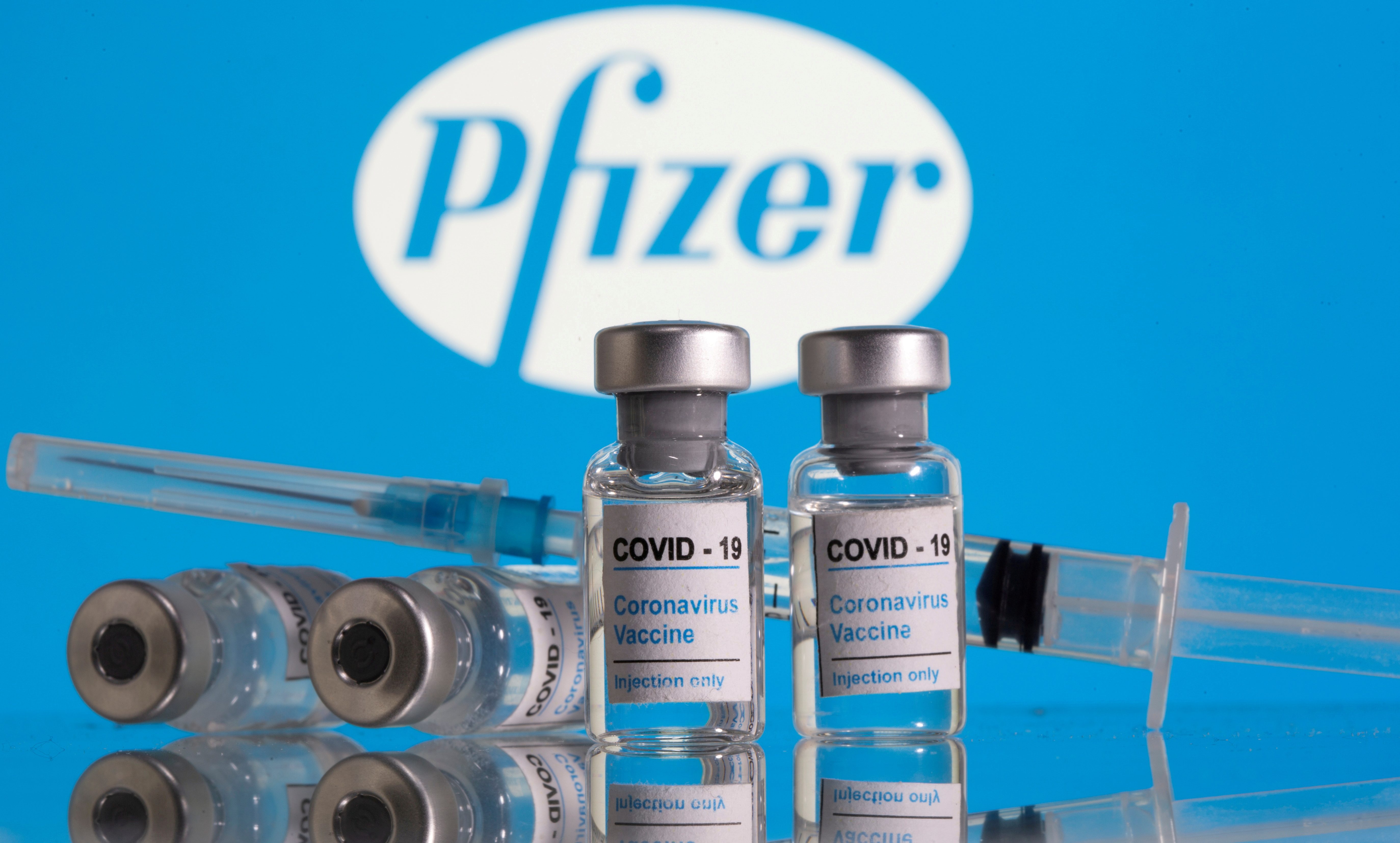 Vials labelled "COVID-19 Coronavirus Vaccine" and a syringe are seen in front of the Pfizer logo in this illustration