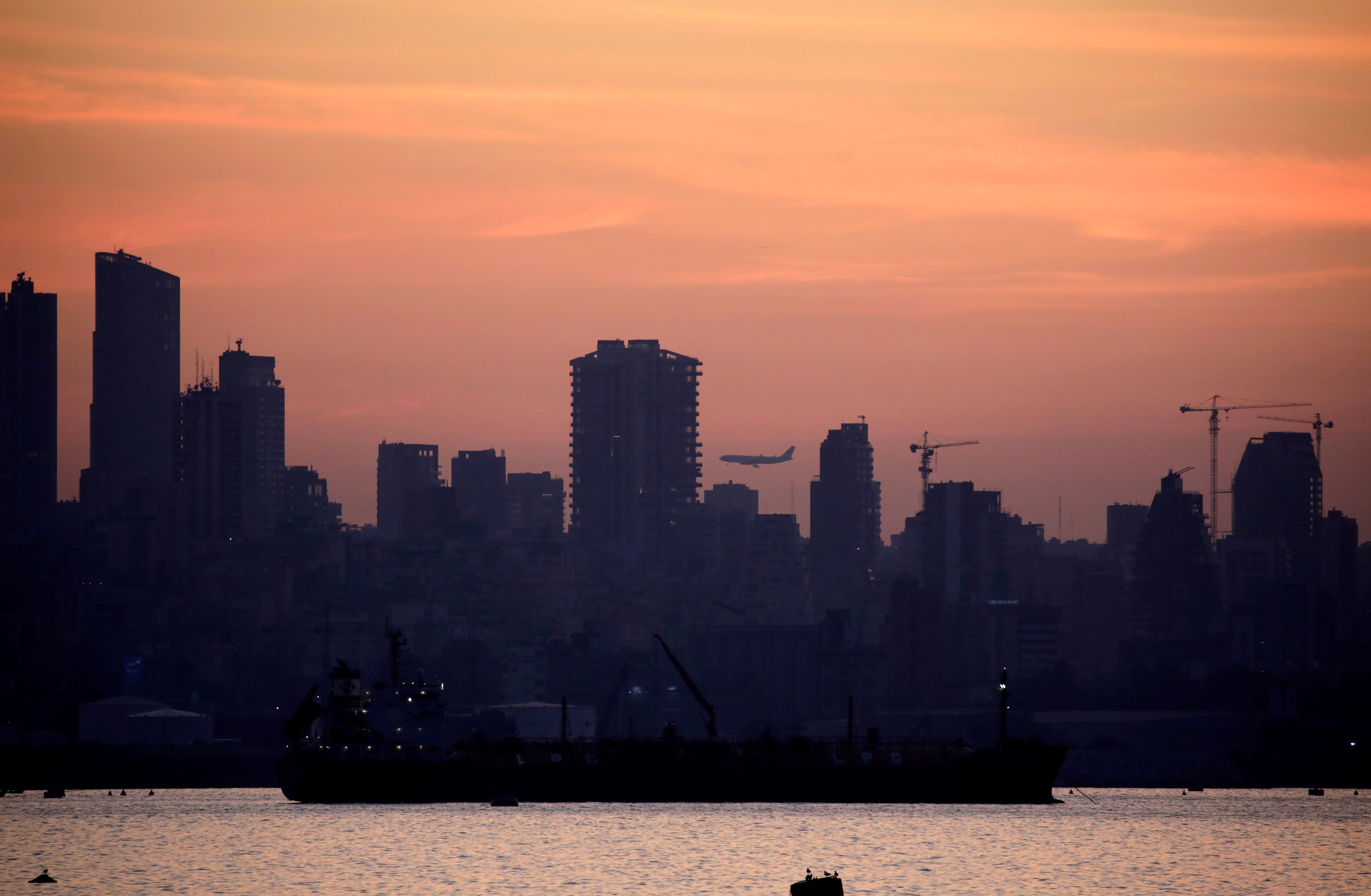 A plane flies as the skyline of Beirut is seen during sunset from Antelias