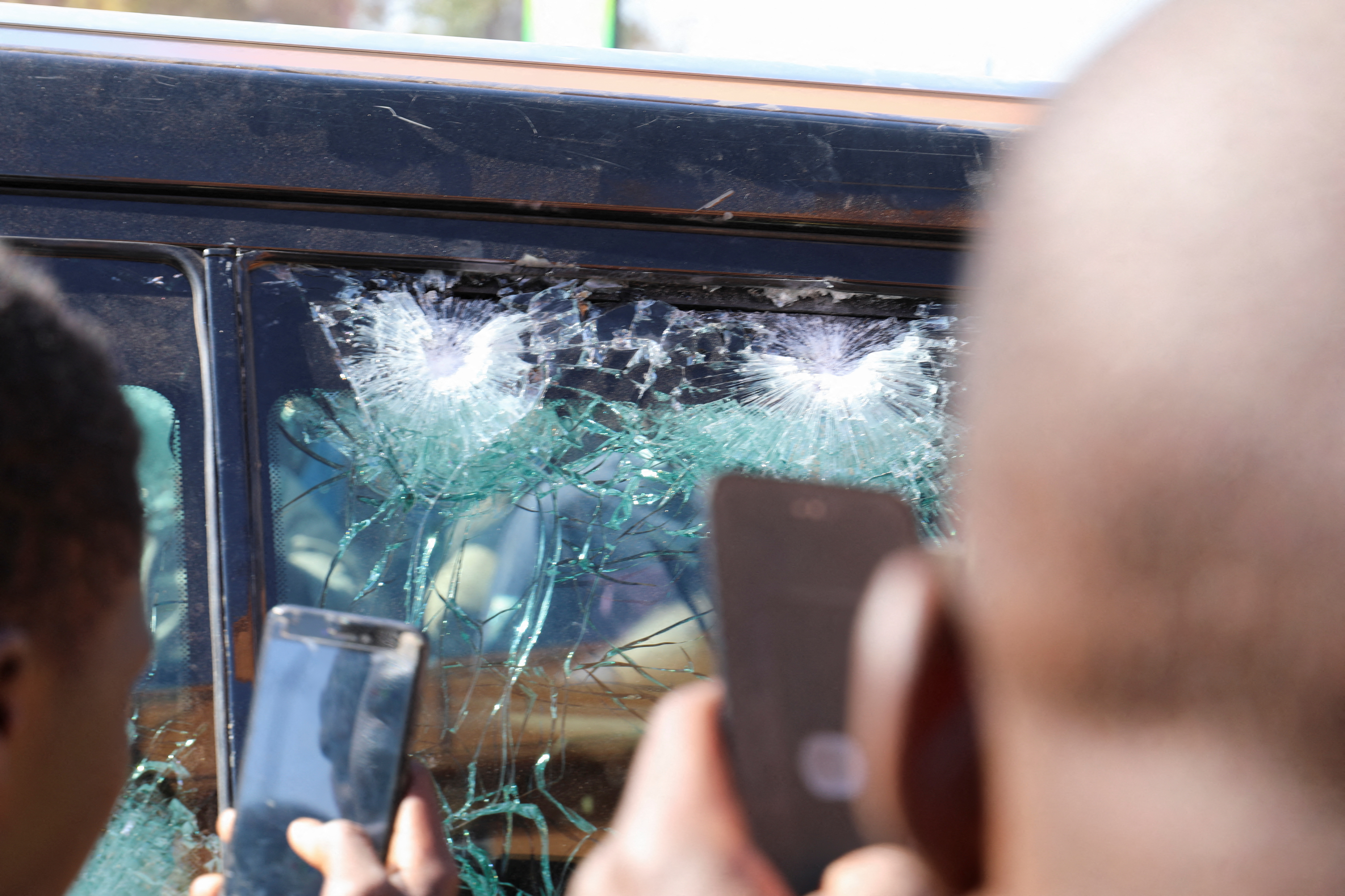 Njerëzit bëjnë fotografi të ndikimit të plumbave në një dritare të automjetit që i përket presidencës pasi Presidenti i Burkina Faso Roch Kabore u ndalua në një kamp ushtarak pas të shtënave të forta pranë rezidencës së presidentit në Ouagadougou, Burkina Faso, 24 janar 2022. REUTERS/ Vincent Bado