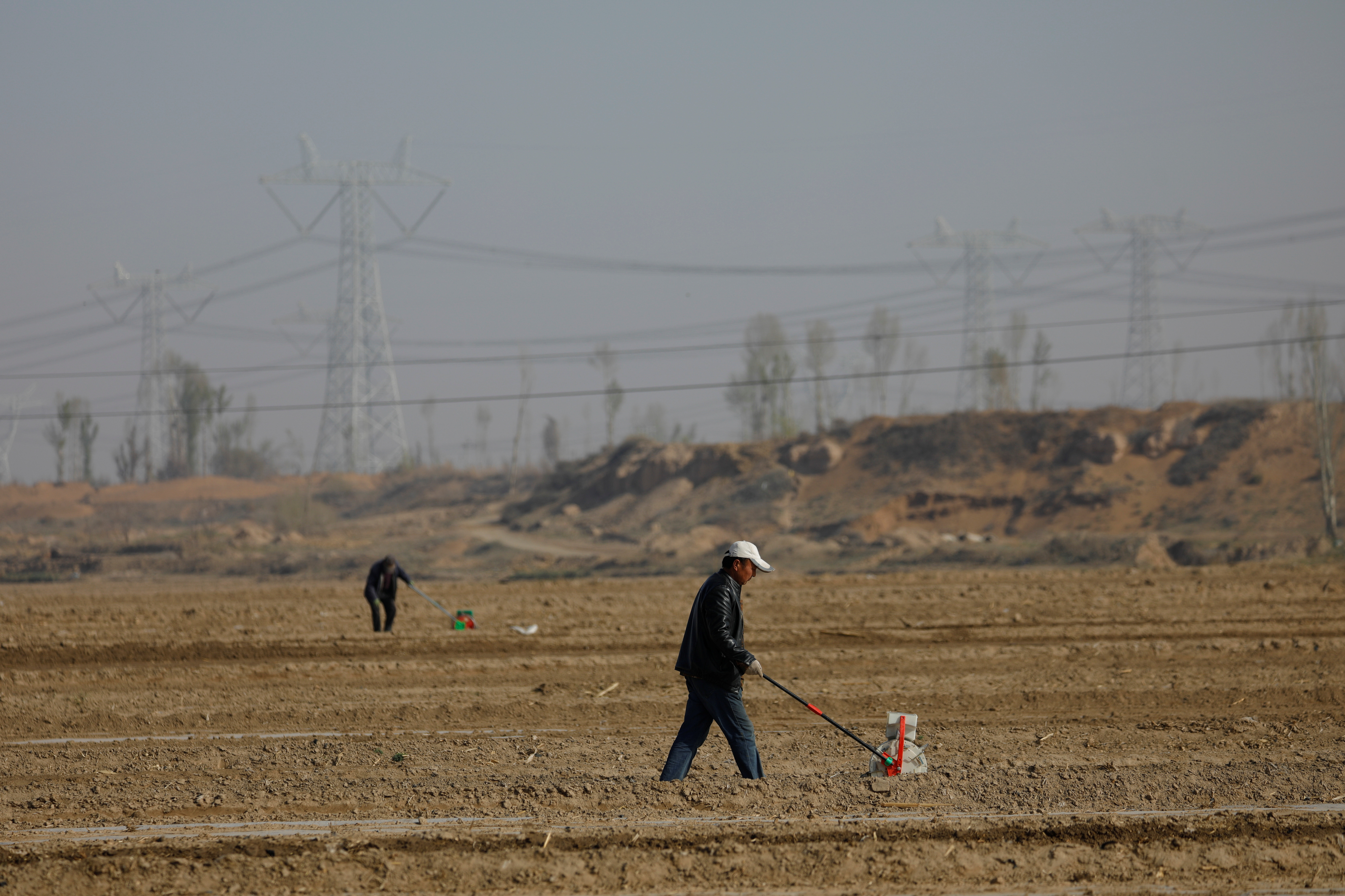 Workers use planters to plant corn seeds on the fields in a village on the outskirts of Wuwei