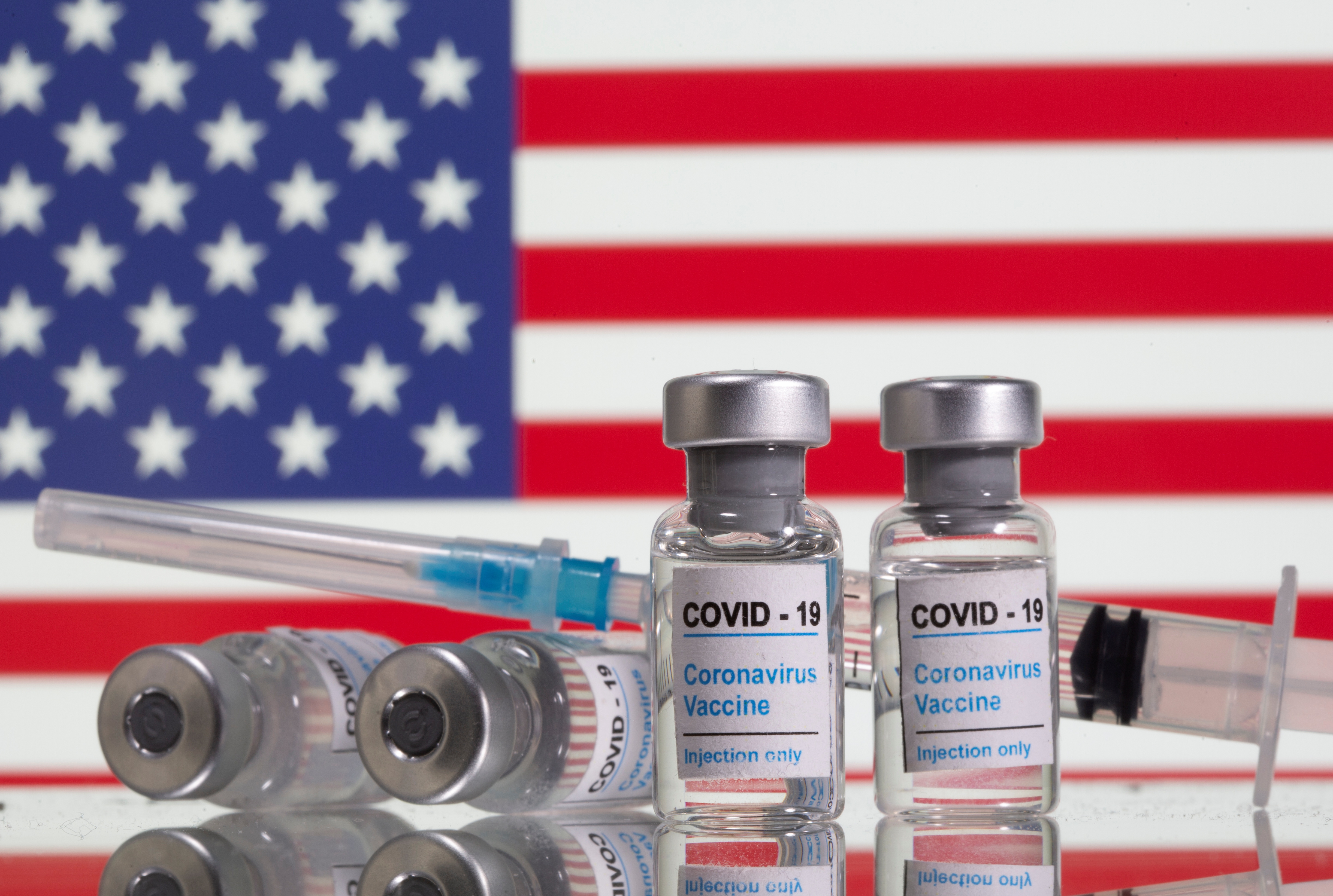 Vials labelled "COVID-19 Coronavirus Vaccine" and sryinge are seen in front of displayed USA  flag in this illustration