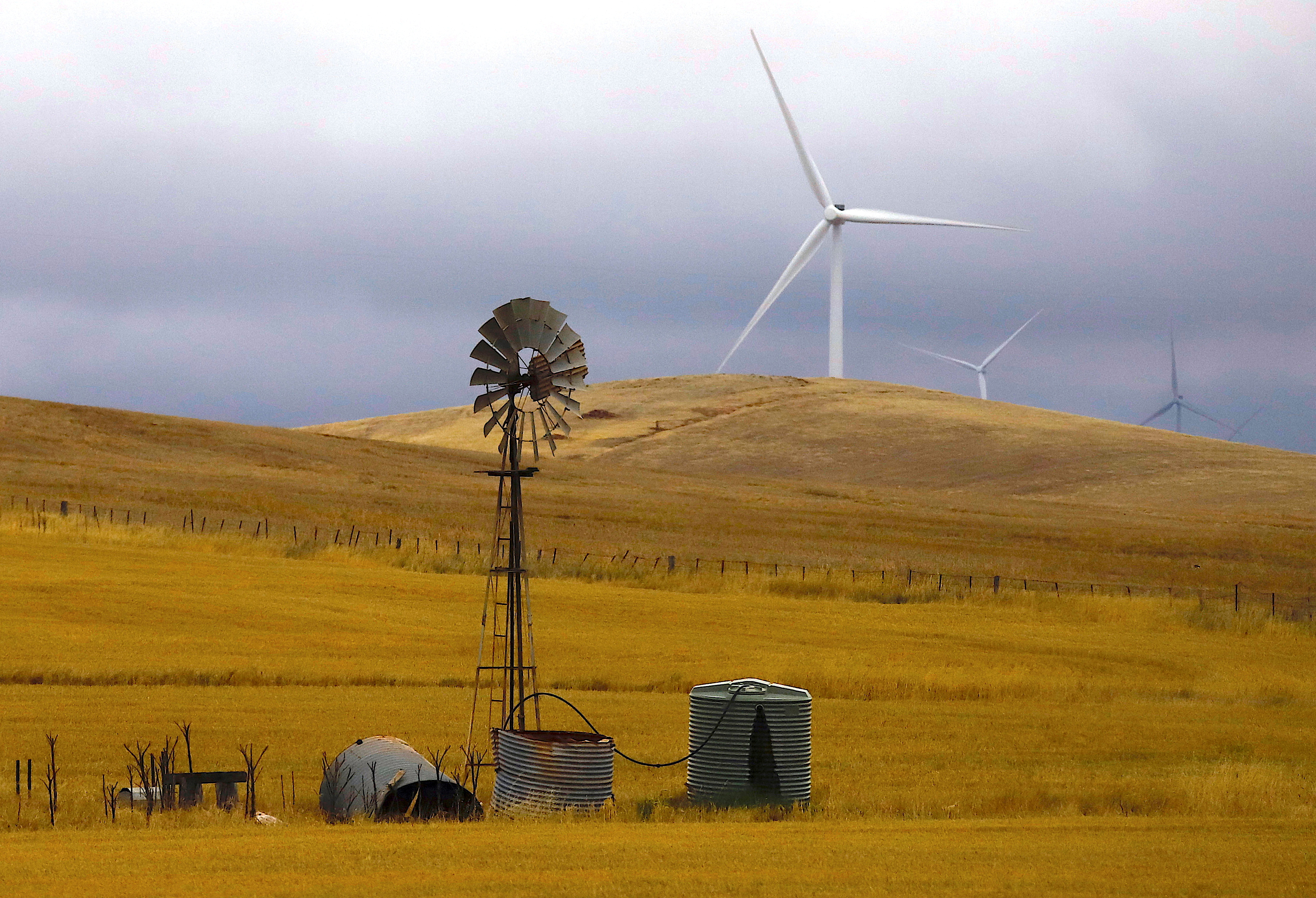 An old windmill stands in front of wind turbines in a paddock near the Hornsdale Power Reserve, featuring the world's largest lithium ion battery made by Tesla, located on the outskirts of the South Australian town of Jamestown