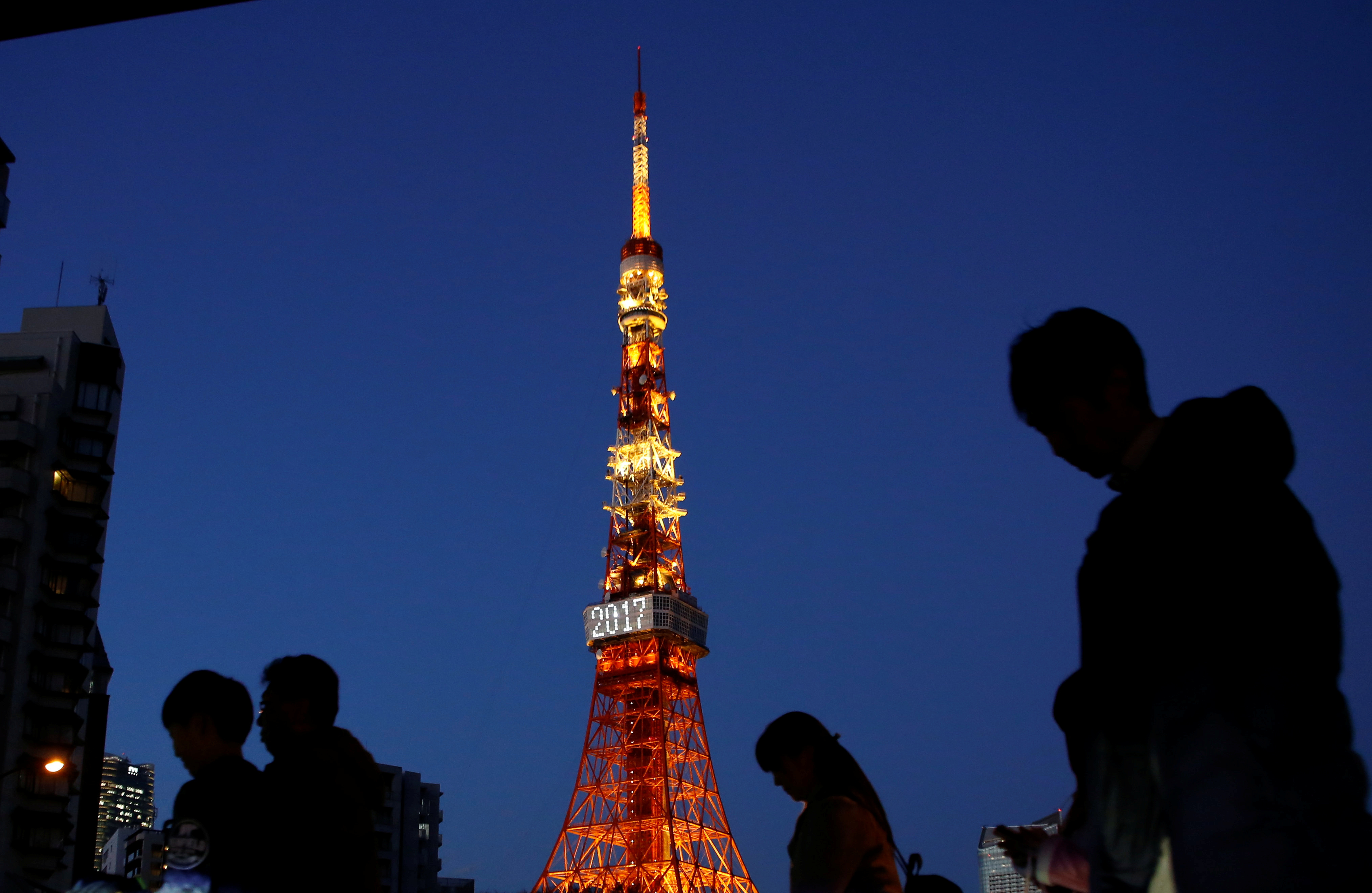 Pedestrians are silhouetted as they walk past the Tokyo Tower in Tokyo