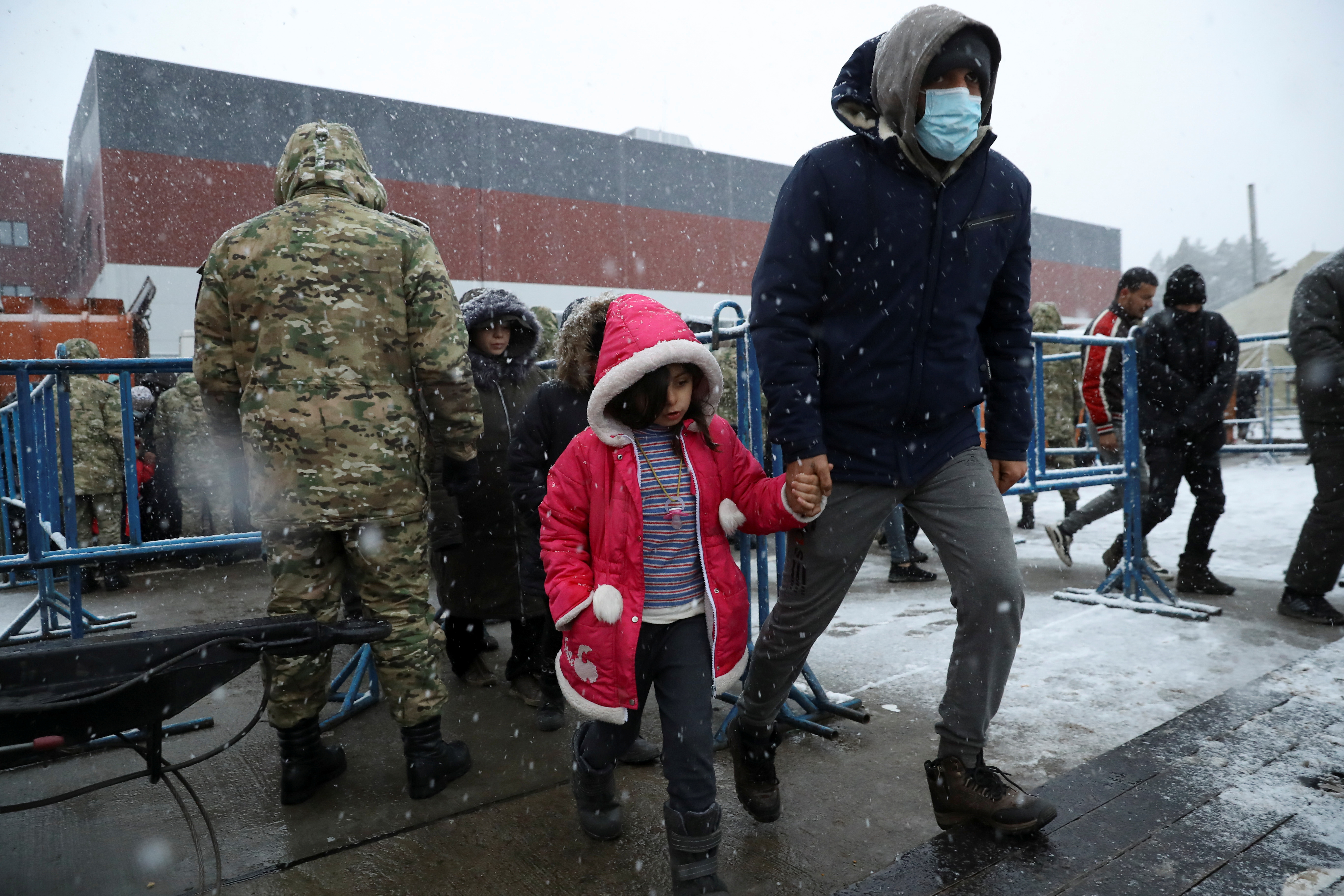A migrant walks with a child during snowfall, at a transport and logistics centre near the Belarusian-Polish border, in the Grodno region, Belarus November 23, 2021. REUTERS/Kacper Pempel